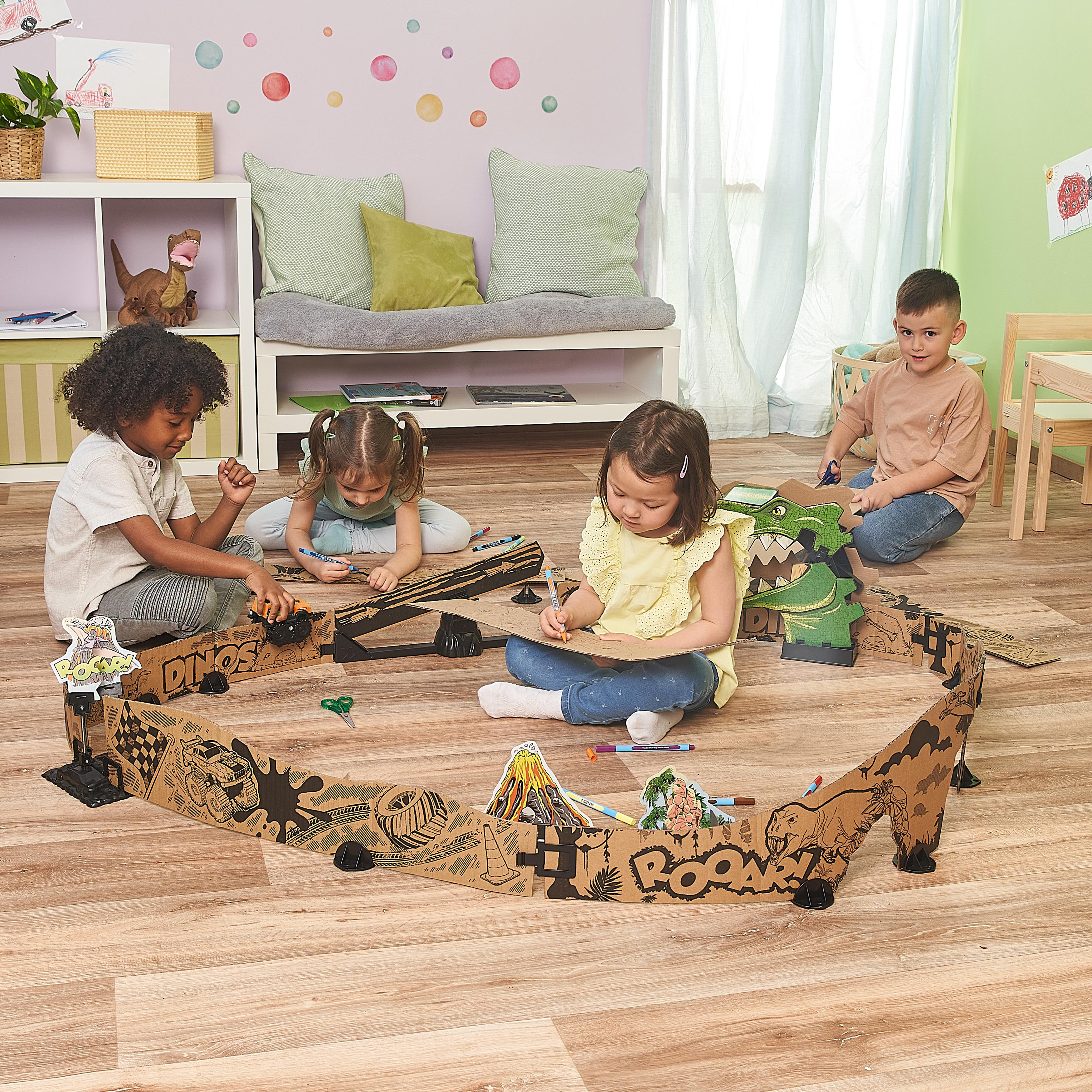 Kinder zeichnen und spielen mit einem Dinosaurier-Aufbau aus Pappe. Sie sind in einem Raum.