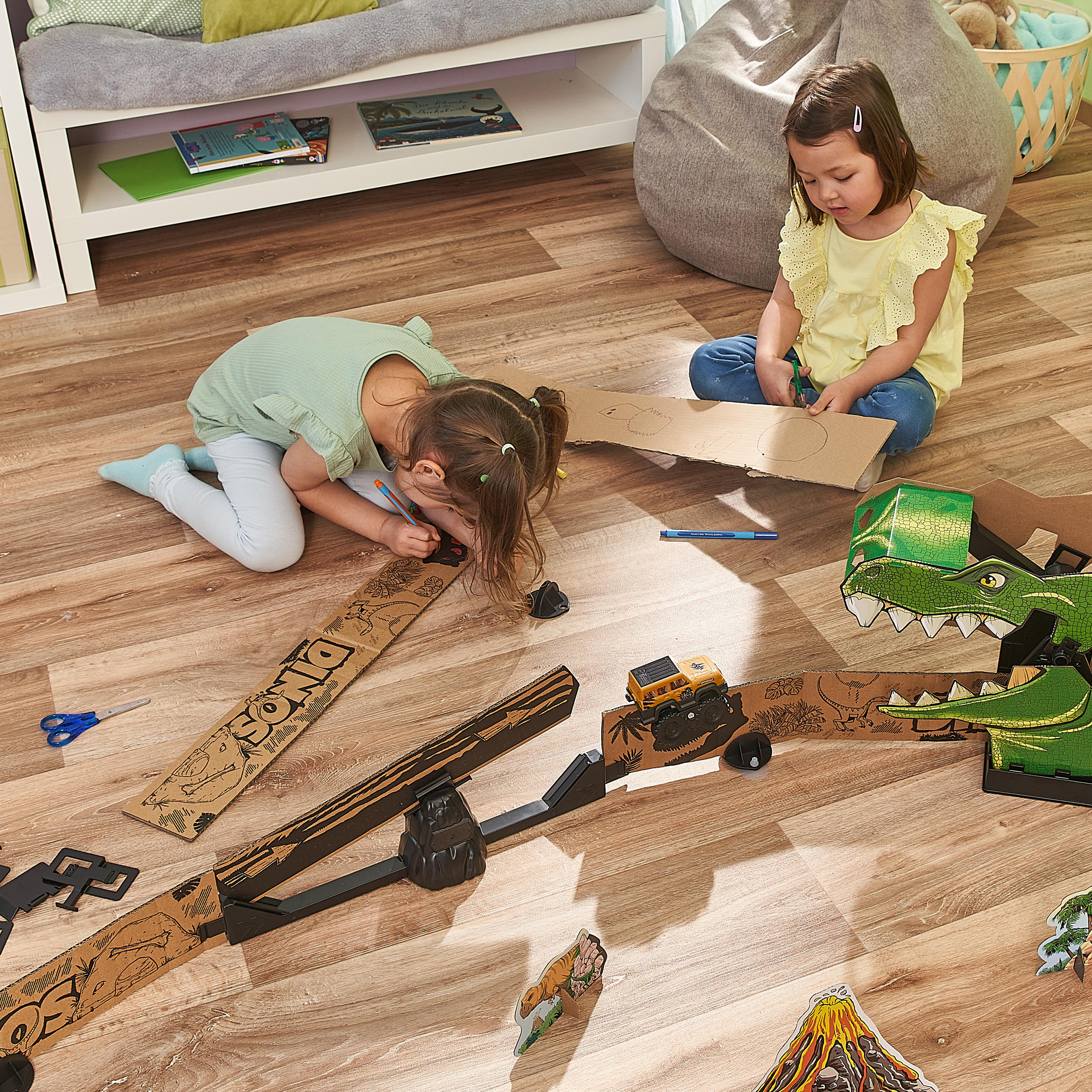 Zwei Kinder zeichnen auf Dinosaurier-Pappe. Holzfußboden.