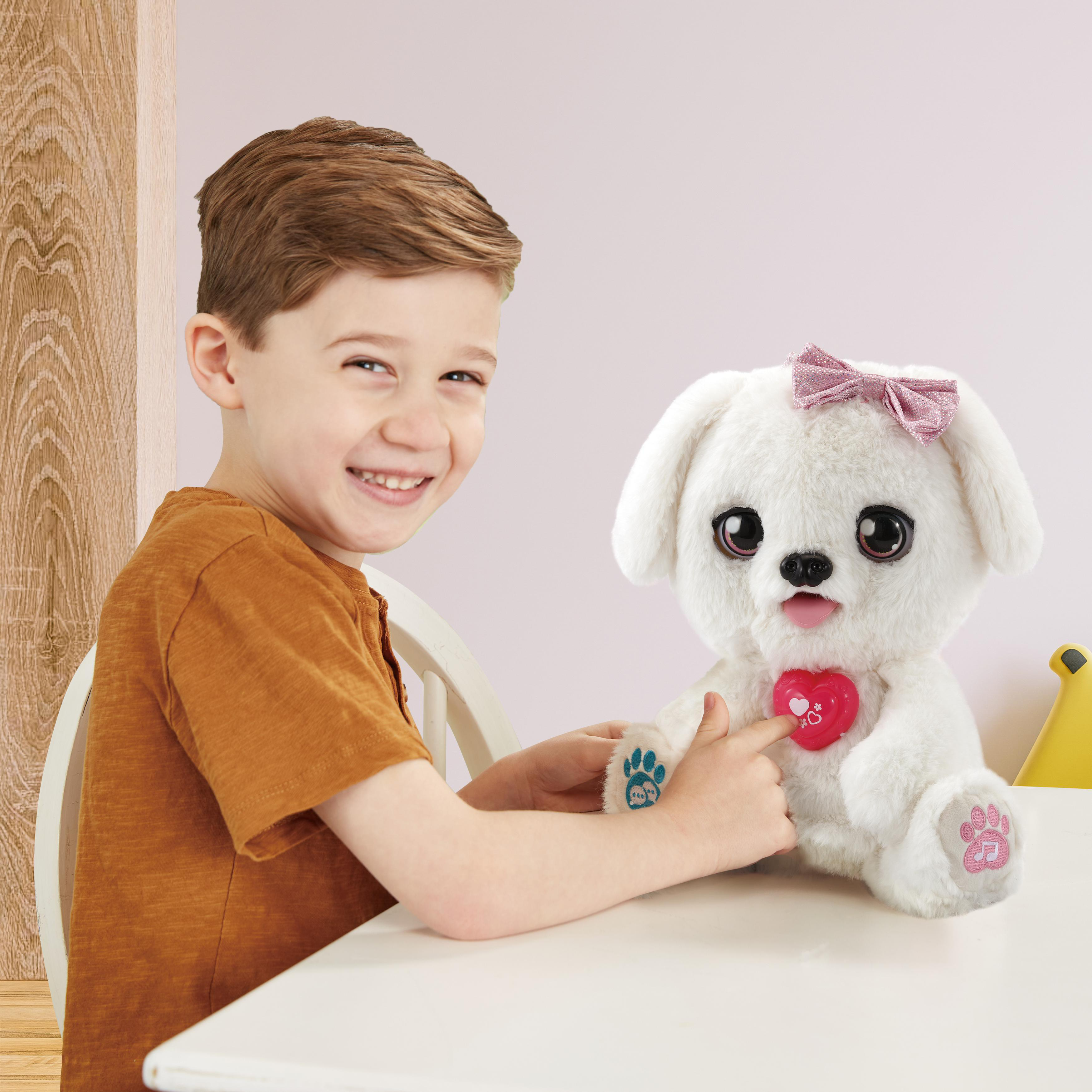 Junge lächelt, zeigt auf weißen Stoffhund. Hund hat rosa Schleife, Herz.