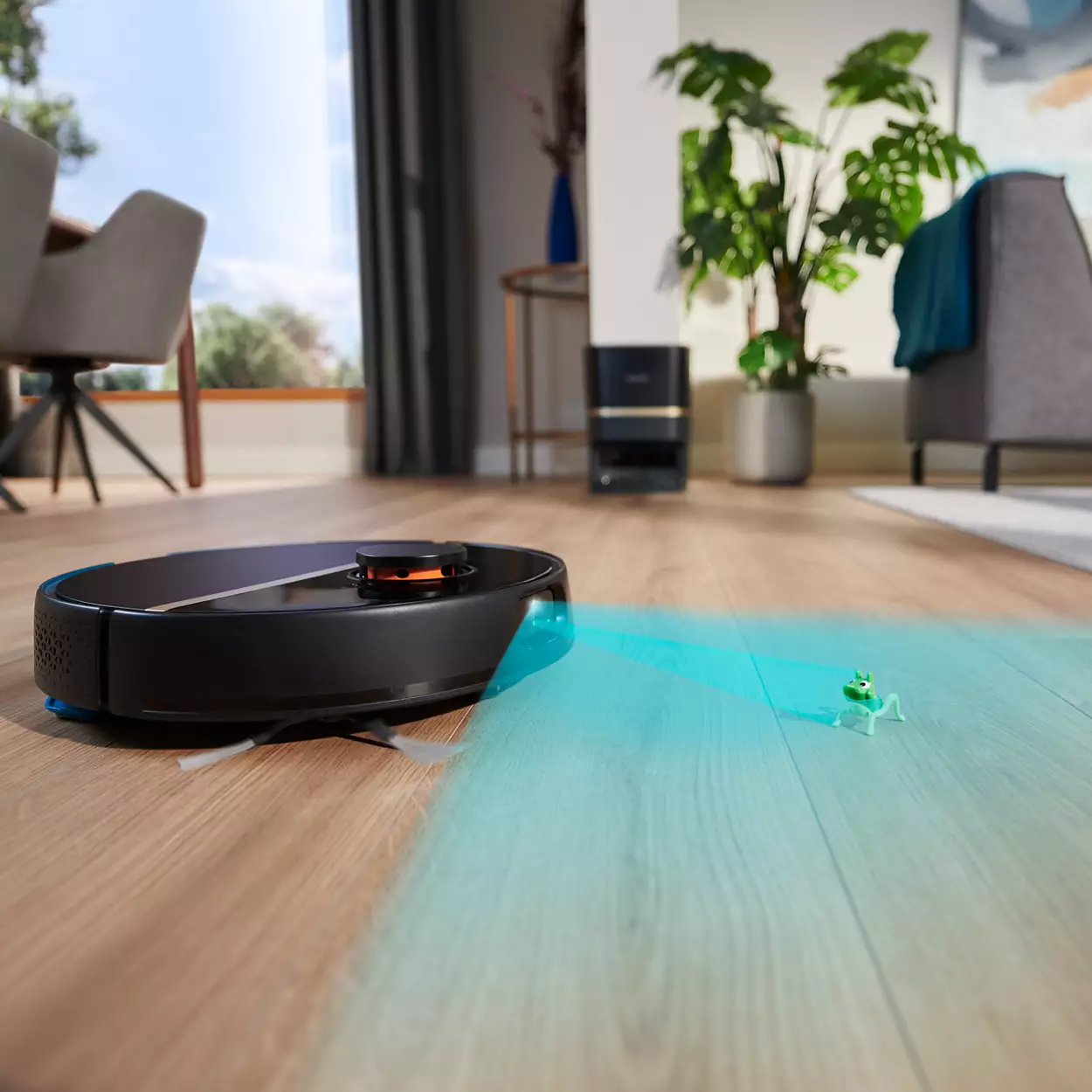 Aspirapolvere robot nero su pavimento in legno. Luce blu proiettata, rana giocattolo.