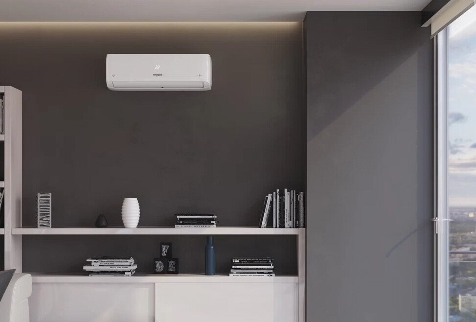 Klimatyzator naścienny znajduje się nad białą półką z książkami i wazonami. Okno znajduje się po prawej stronie.