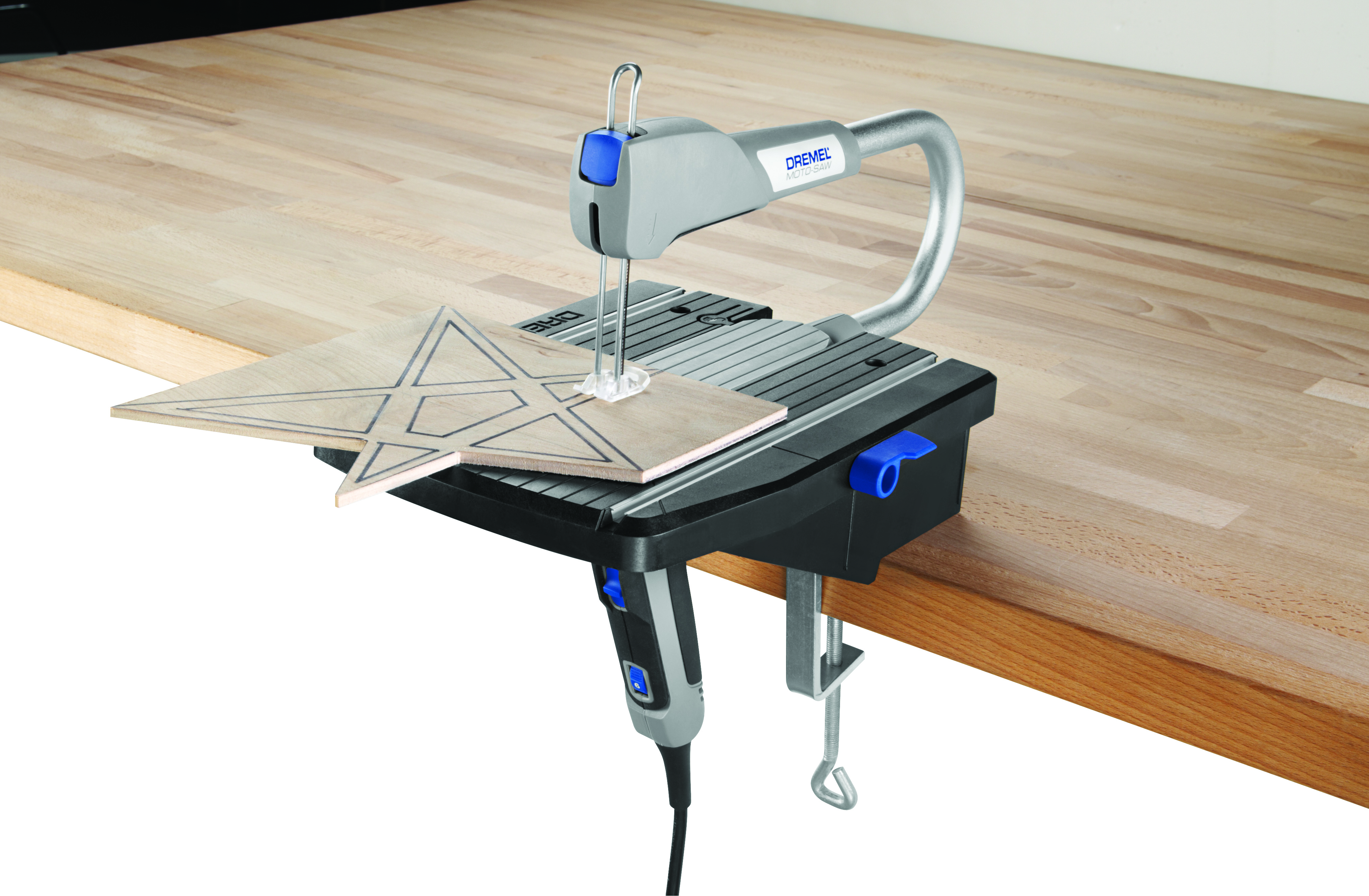 Dremel szúrófűrész csillagformát vág fából. A fűrész fekete-szürke, fa asztalon.