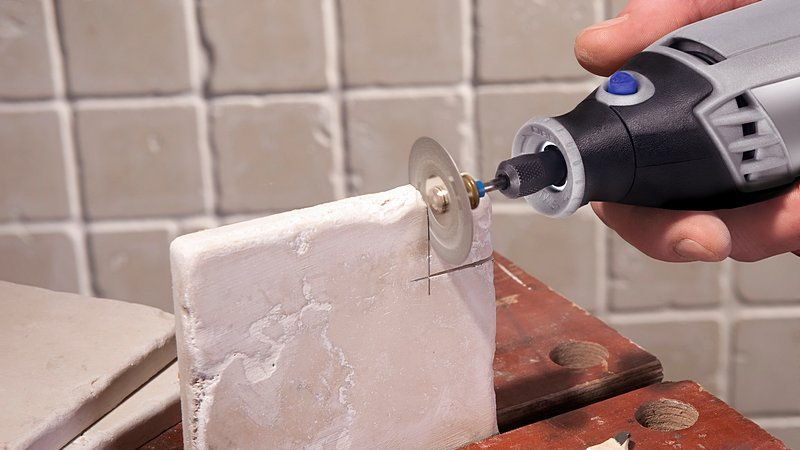 Kéz Dremel forgószerszámot használ a horony vágásához egy világos téglatestben.