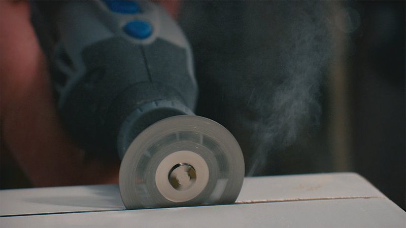 Egy Dremel szerszám hornyot vág egy fehér felületbe, port generálva.