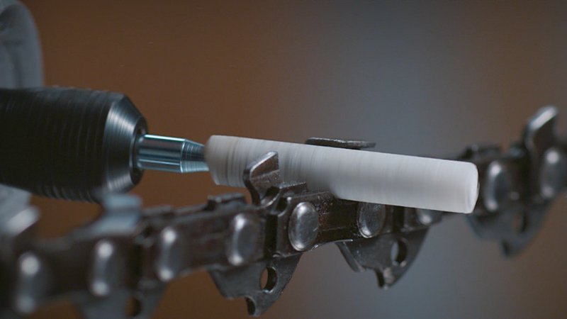 Egy Dremel szerszám élesíti a láncfűrész lapját, közelkép a vágófogakról.