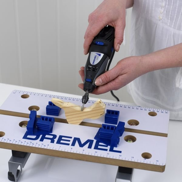 Személy Dremel szerszámot használ fán. Asztal kapcsokkal és tartókkal.