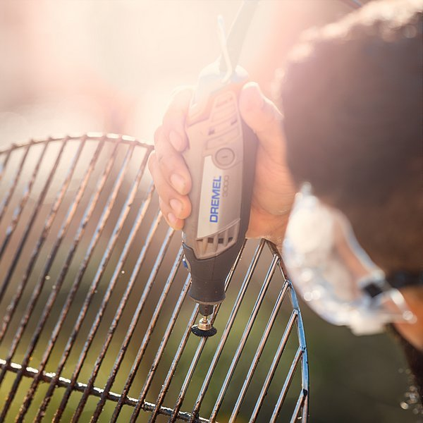 Személy Dremel eszközzel tisztít egy grillsütőt. A szerszámon egy kis kefefej van.