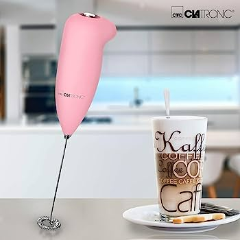 Rózsaszín kézi mixer a Clatronic márkától, egy kávés itallal teli pohár és egy süteményes tányér mellett.