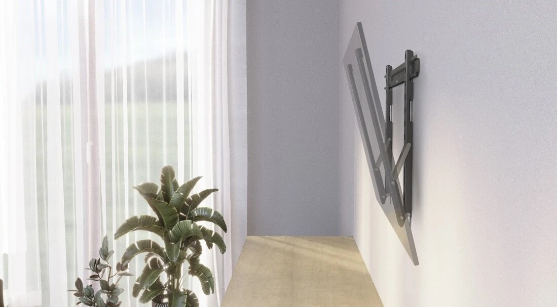 Telewizor zamontowany na ścianie z uchwytem. Biała ściana i przezroczysta zasłona.