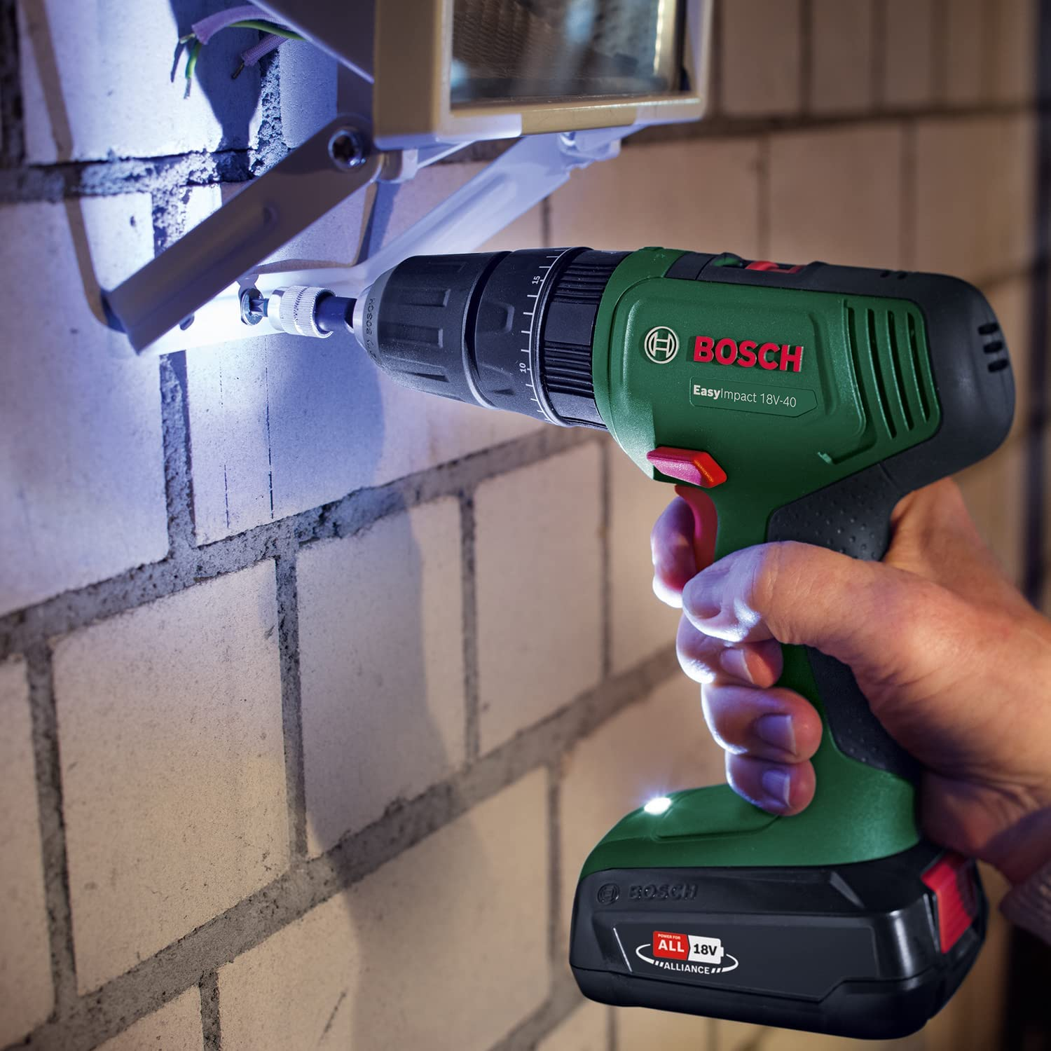 Férfi zöld Bosch Easyimpact 18V-40 fúróval szerel szerelvényt téglára.