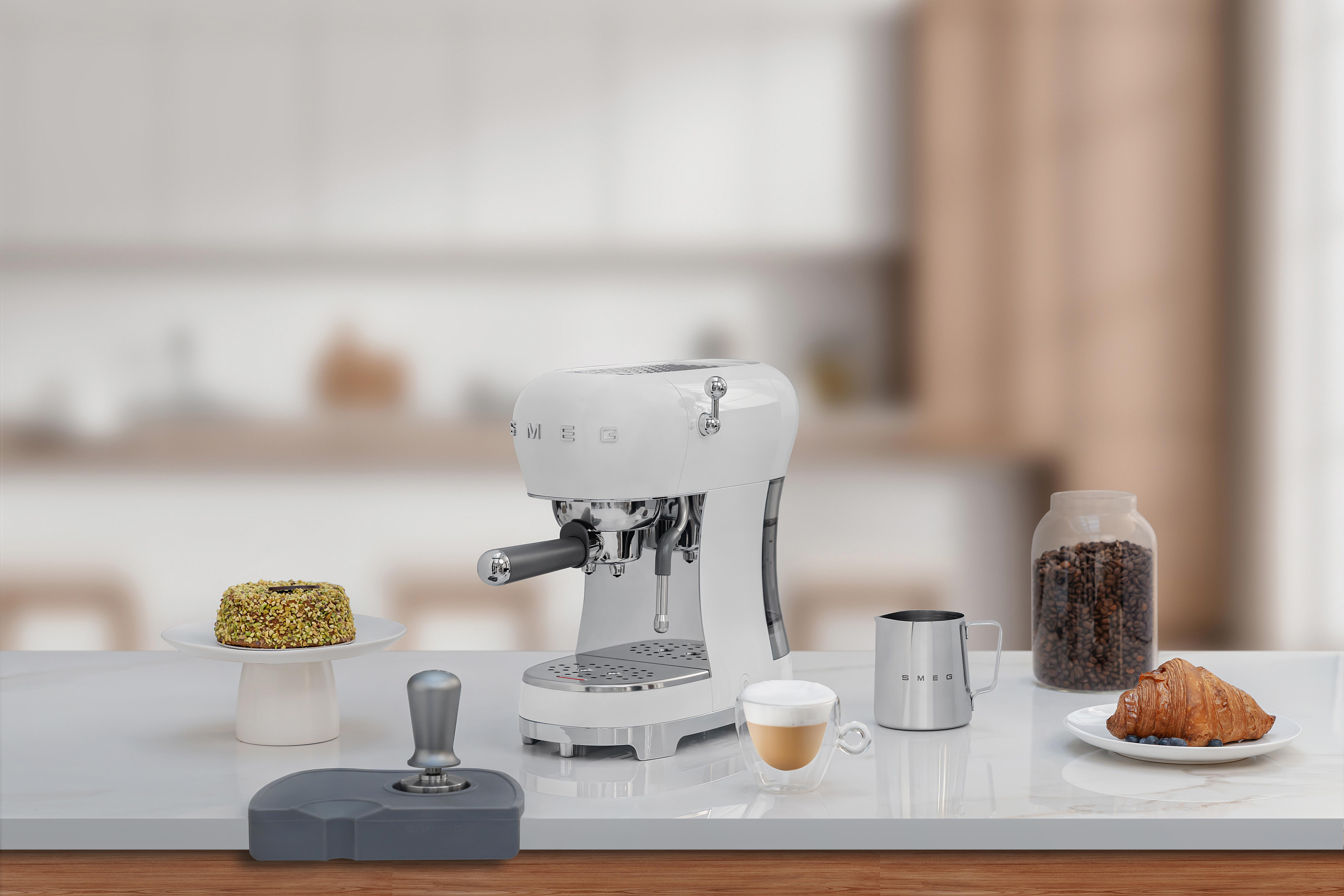 Weiße SMEG Espressomaschine mit Zubehör auf weißer Arbeitsplatte.