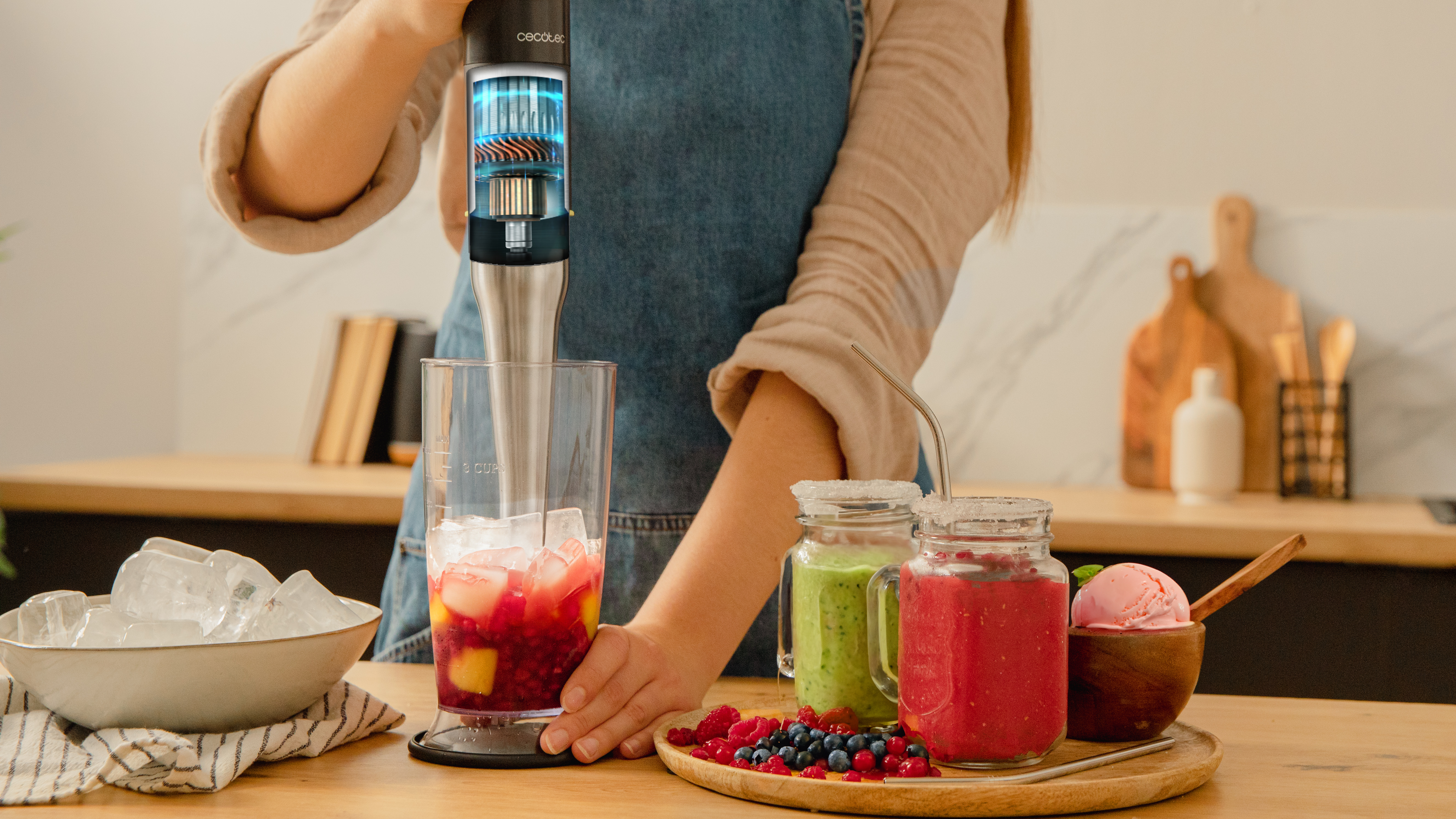 Persona mezclando bebida con batidora de inmersión, con hielo, frutas y batidos.