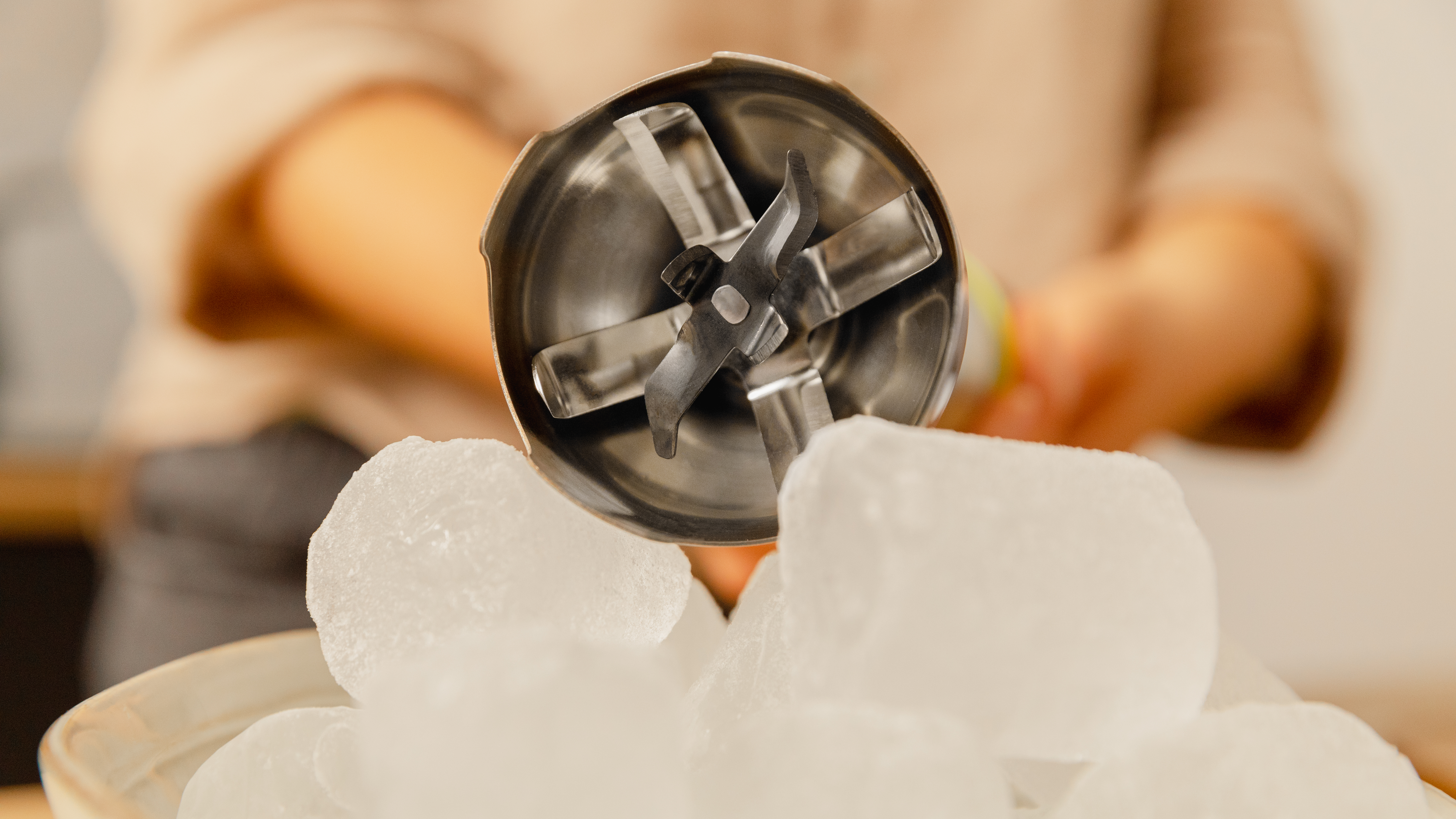 Una batidora de inmersión sobre cubitos de hielo en un cuenco. Las cuchillas de la batidora son visibles.