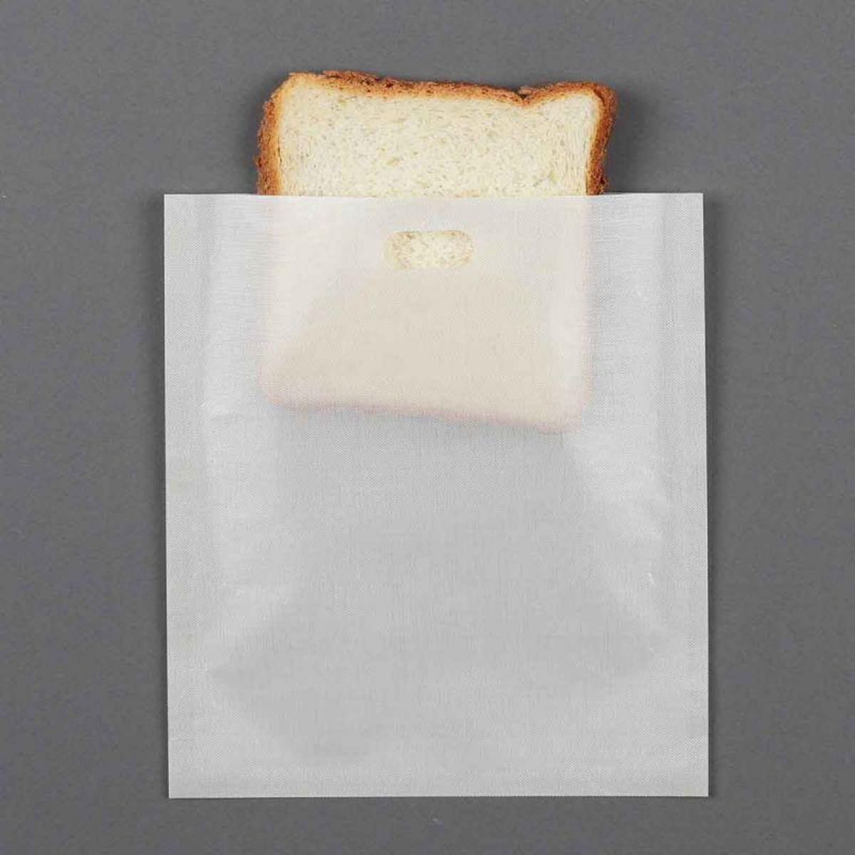 Una rebanada de pan sobresale de una bolsa de papel blanca. La bolsa está sobre un fondo gris.