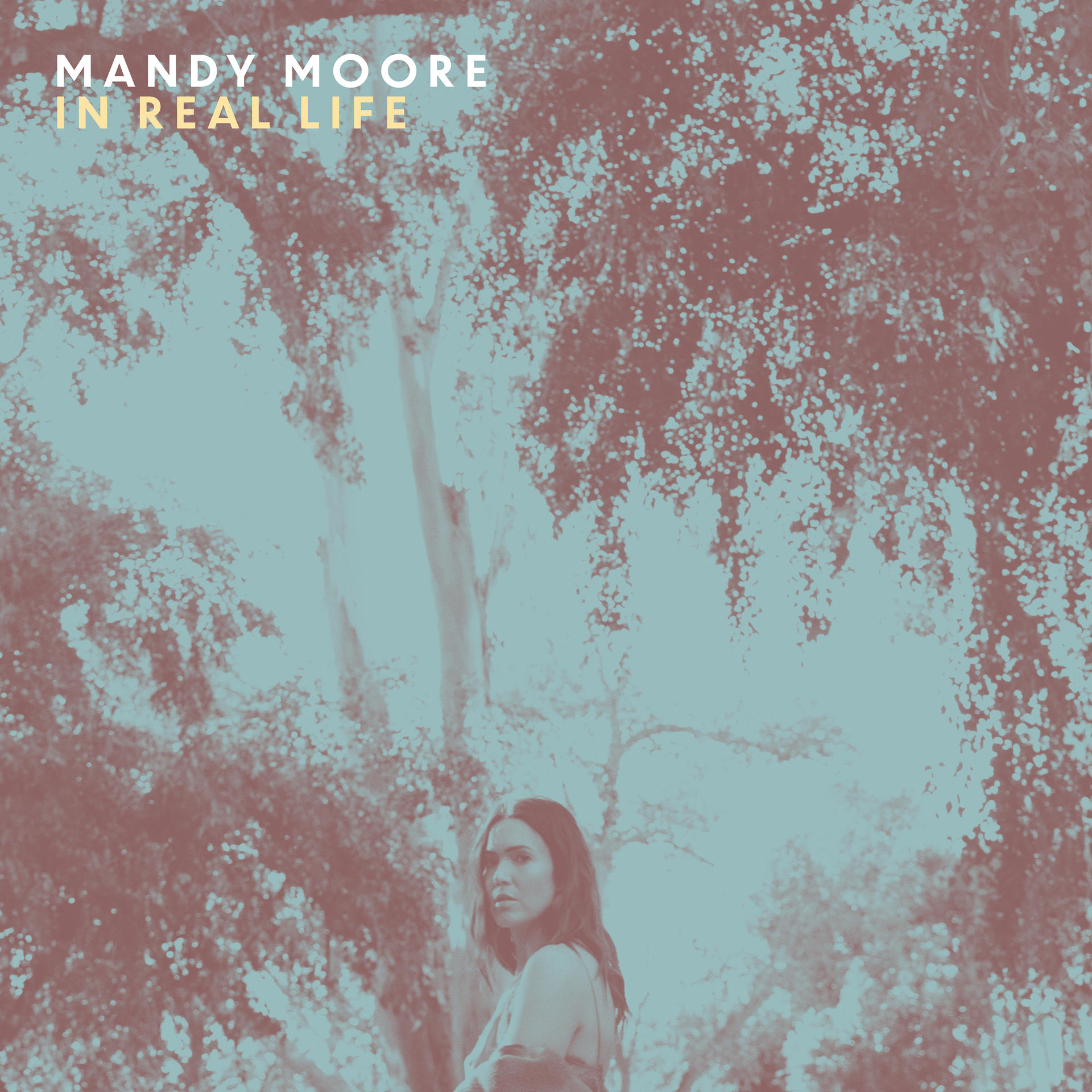 Album borító a "MANDY MOORE IN REAL LIFE" szöveggel és egy fotó Mandy Moore-ról egy erdei környezetben.