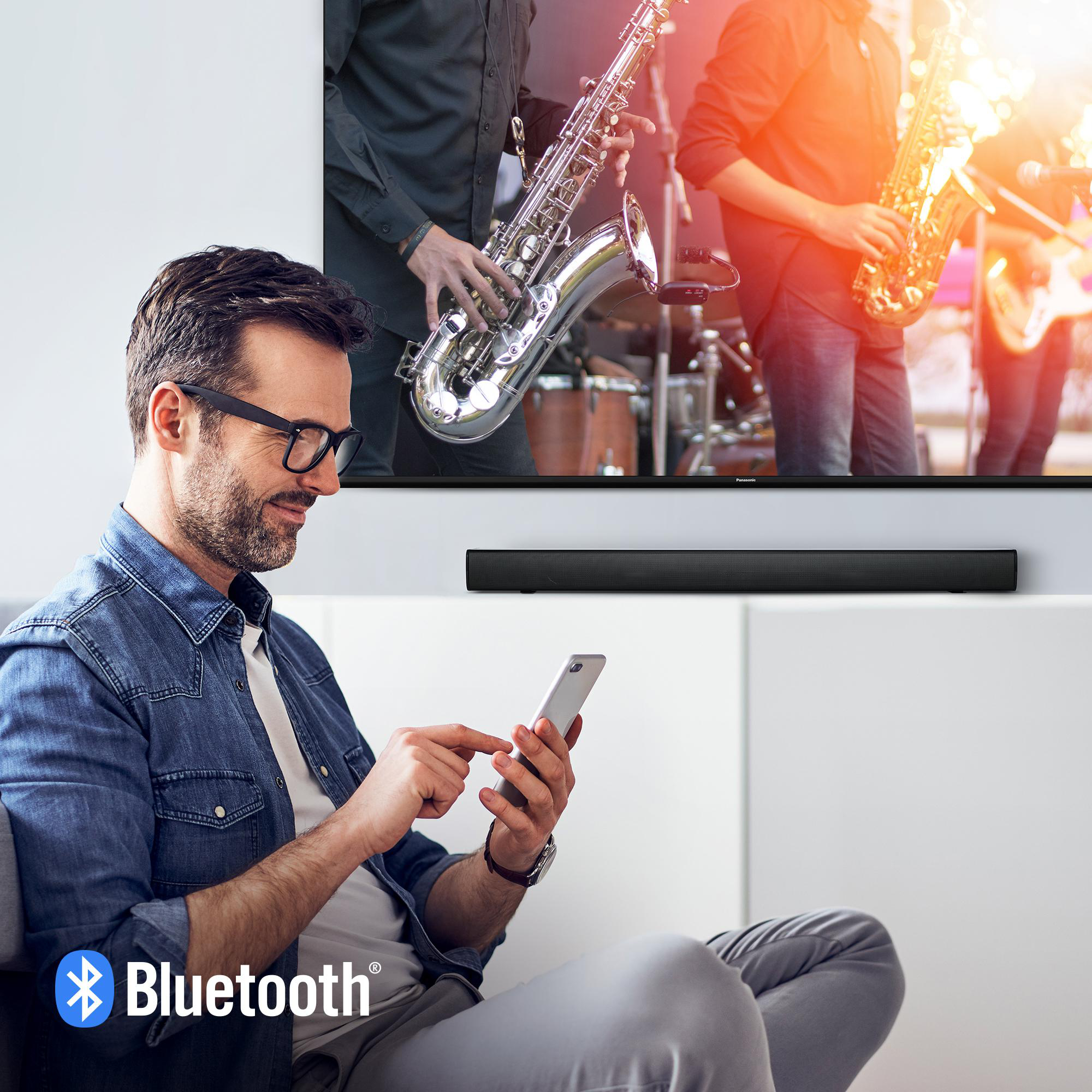 Mann mit Brille benutzt Telefon, Soundbar unter TV, Musiker auf dem Bildschirm.