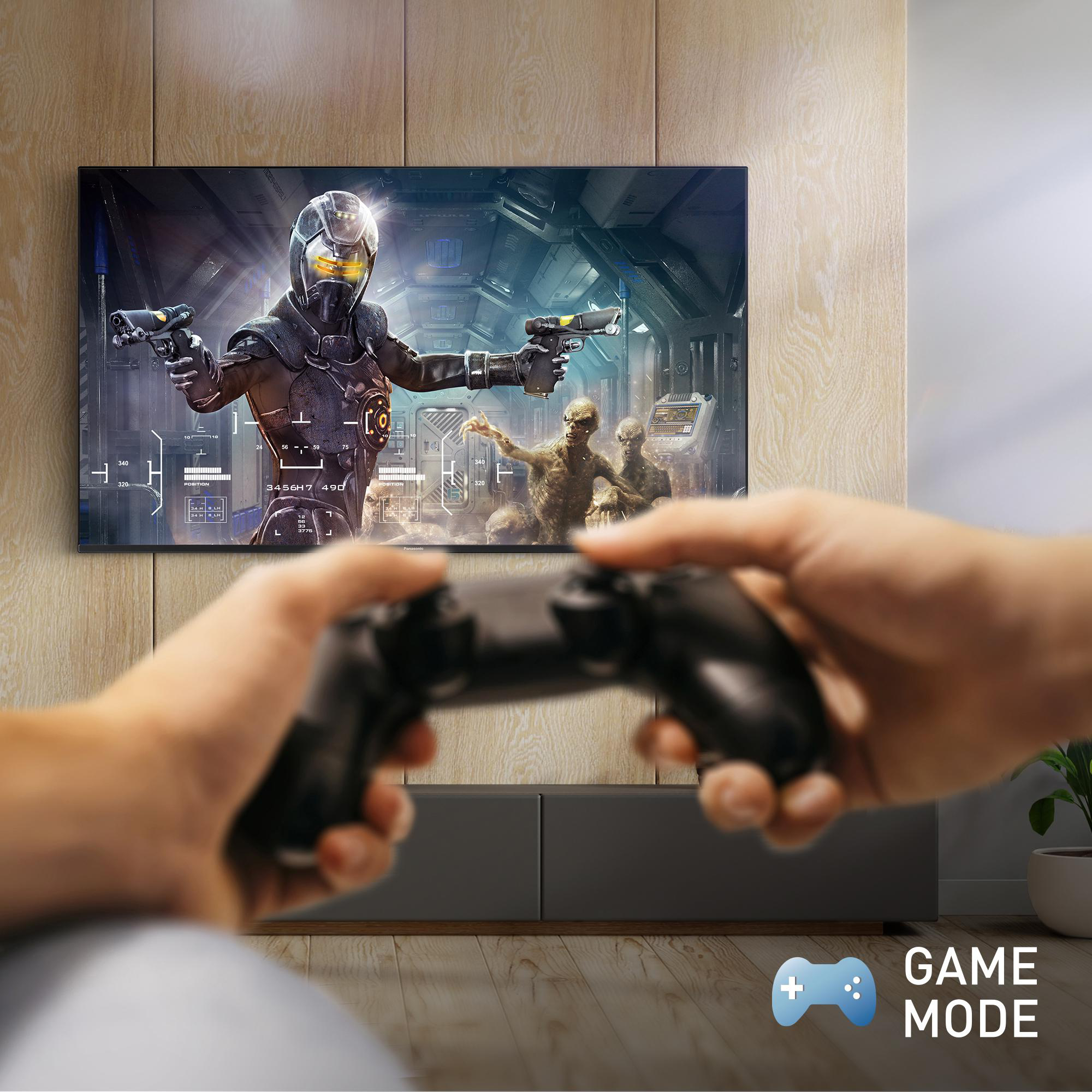 Person hält Controller, spielt Spiel auf Fernseher. Game-Modus-Symbol sichtbar.