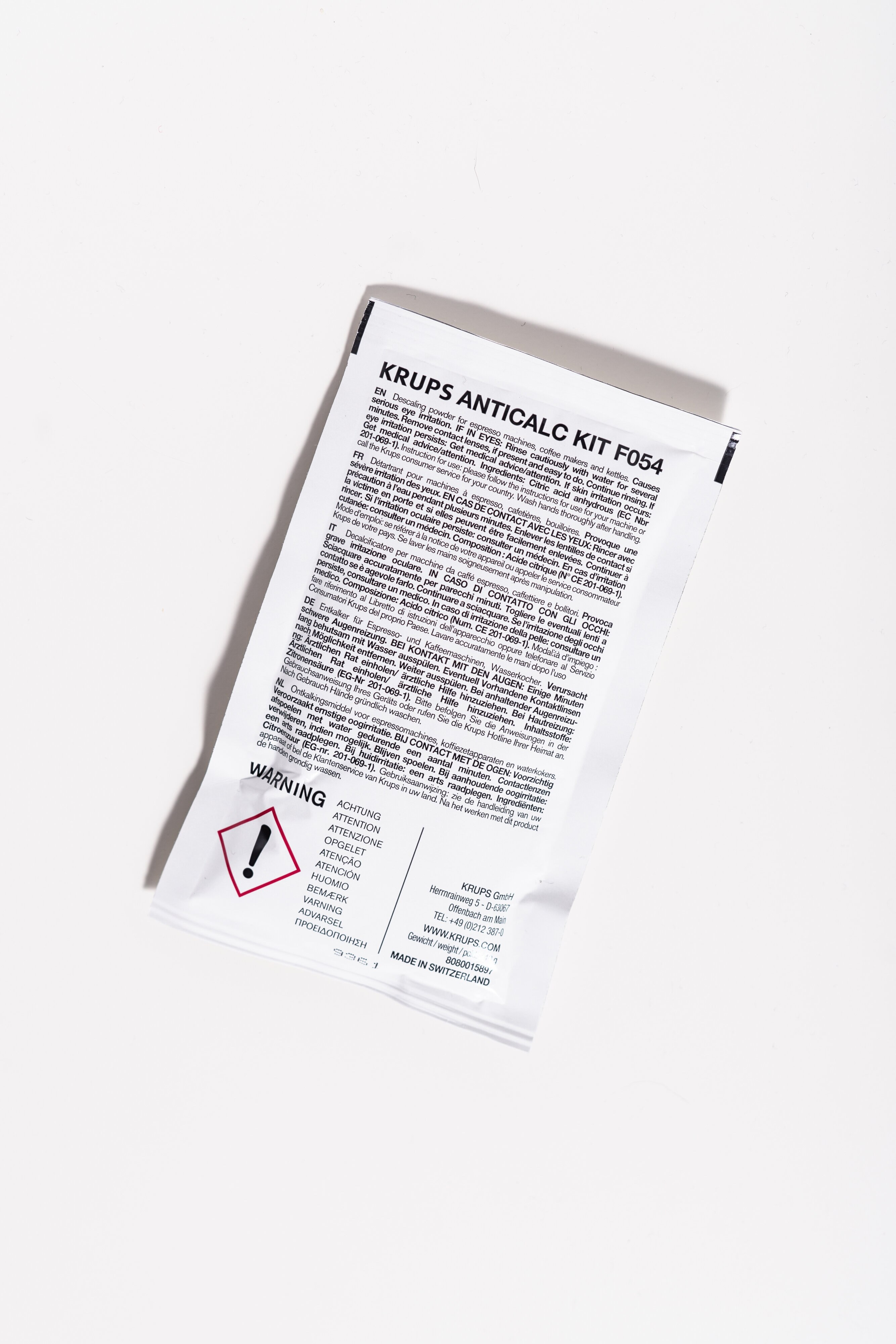 Biała saszetka z tekstem, wykrzyknikiem i symbolem ostrzegawczym.