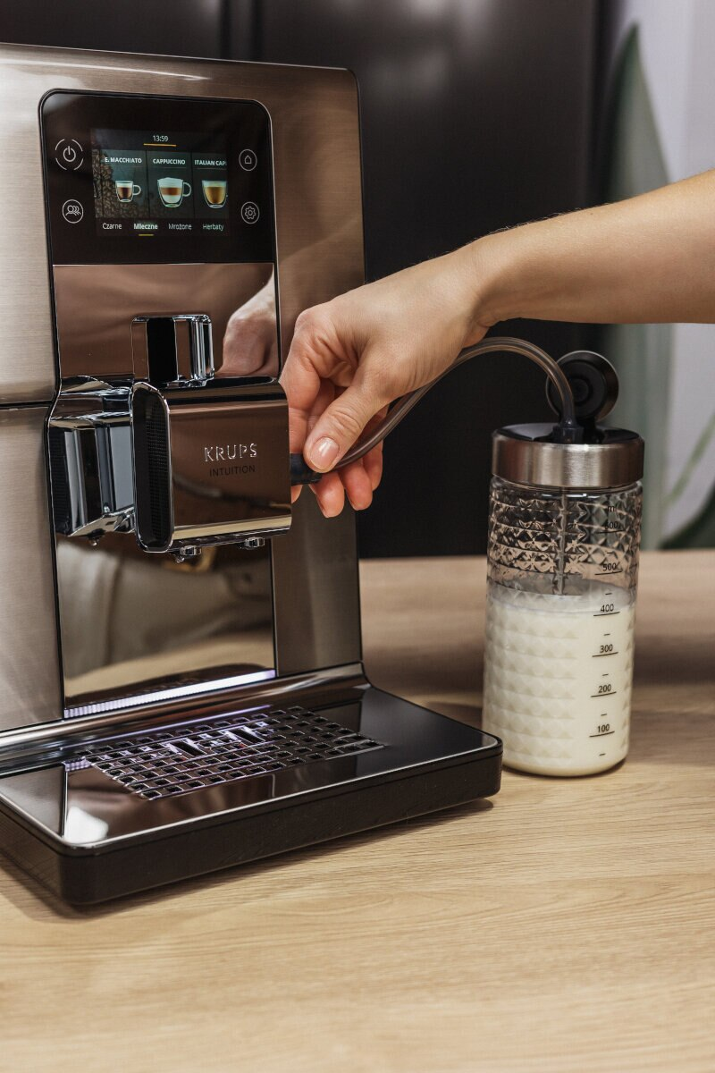 Osoba używa ekspresu do kawy Krups. Mleko jest dodawane do pojemnika do spieniania.