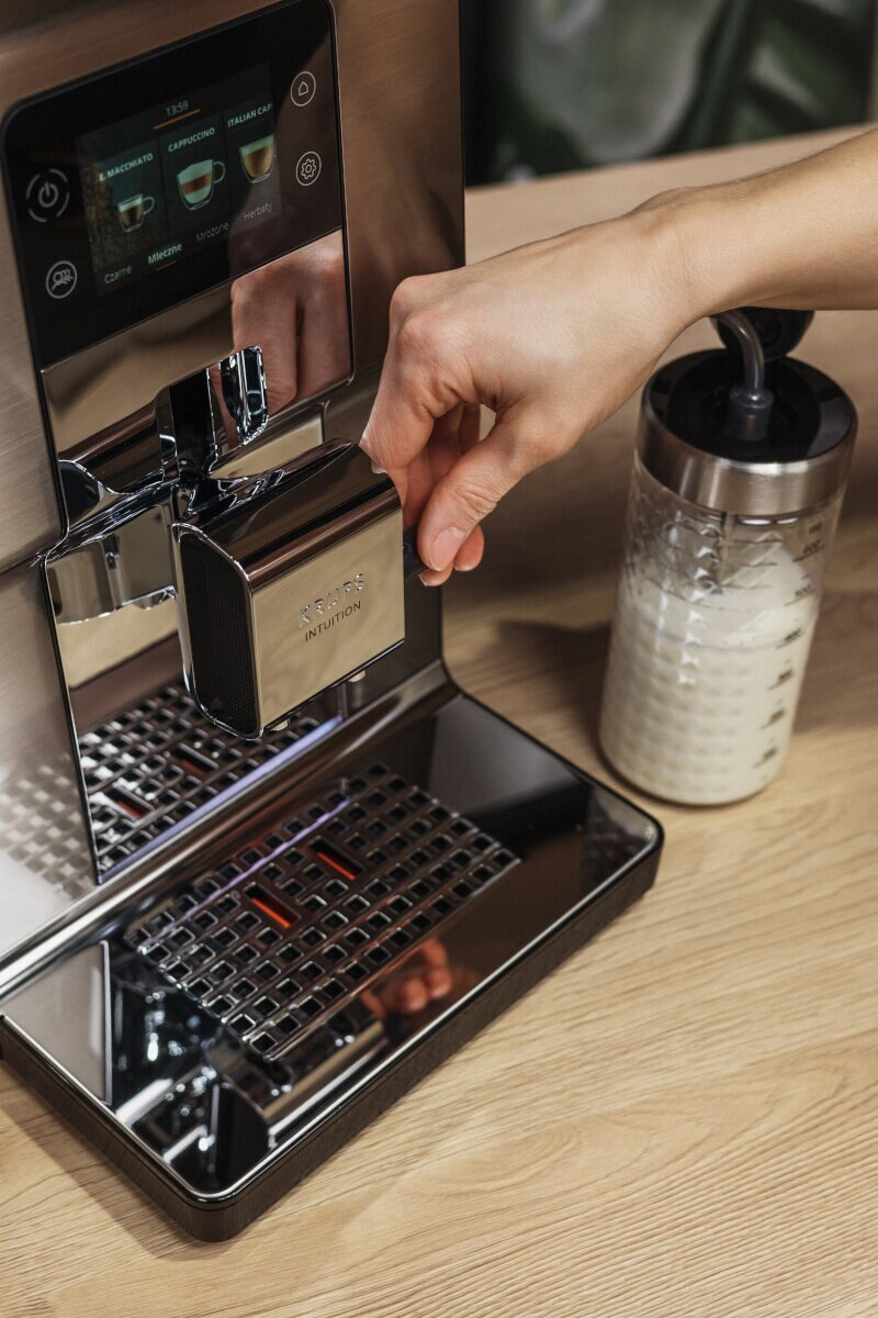 Osoba korzystająca z ekspresu do kawy Krups Intuition, ze zbiornikiem na mleko.
