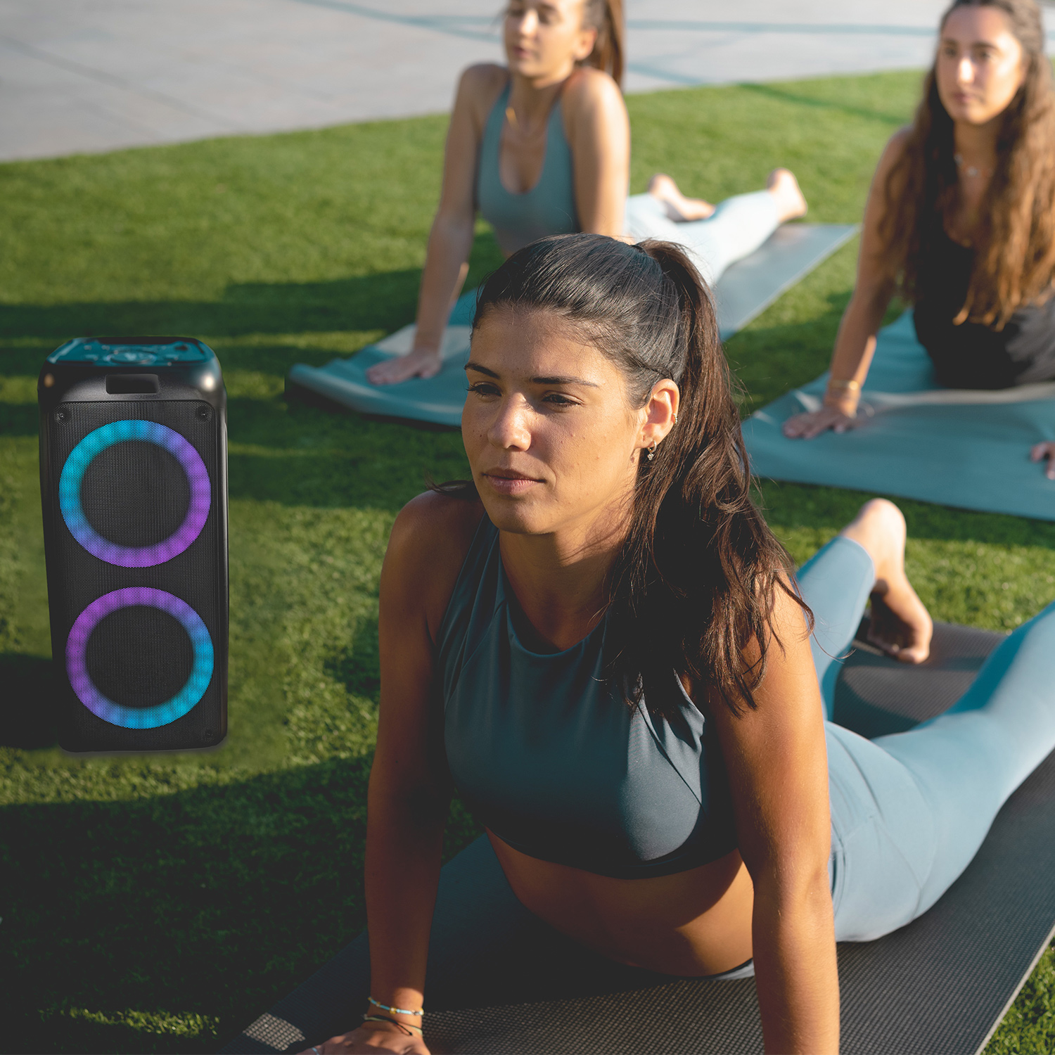 Tres mujeres haciendo yoga en esterillas cerca de un altavoz con luces de colores.