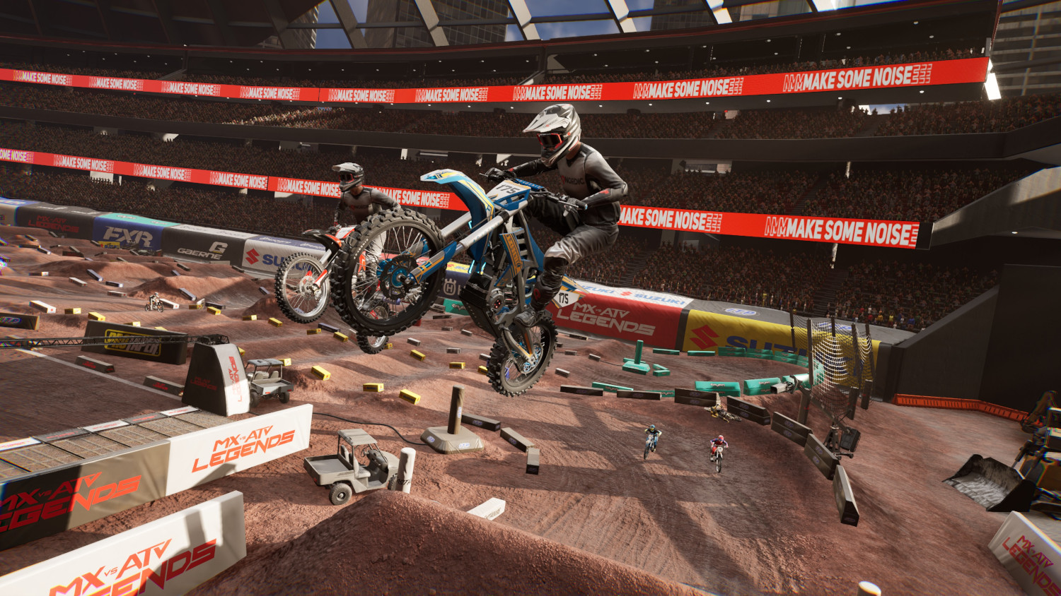 Motorcrossers op motoren in de lucht in een stadion tijdens een race. De scène is vol actie.