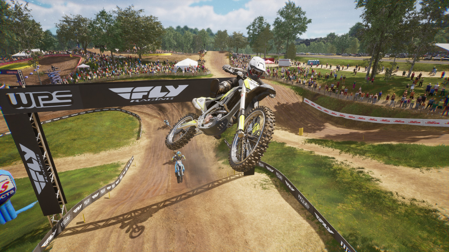 Een motorcrosser springt over een zandbaan. Toeschouwers kijken. De baan heeft een banner met FLY RACING.