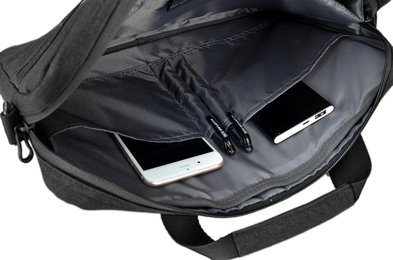 Offene schwarze Laptoptasche mit Telefon, Stiften und Powerbank. Innenraum hat Taschen und einen Riemen.