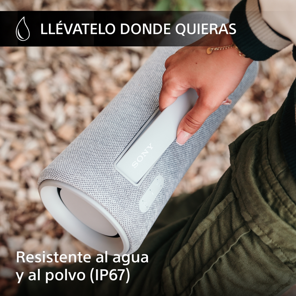 Una persona sostiene un altavoz Sony gris claro, cerca de un fondo borroso verde y gris.
