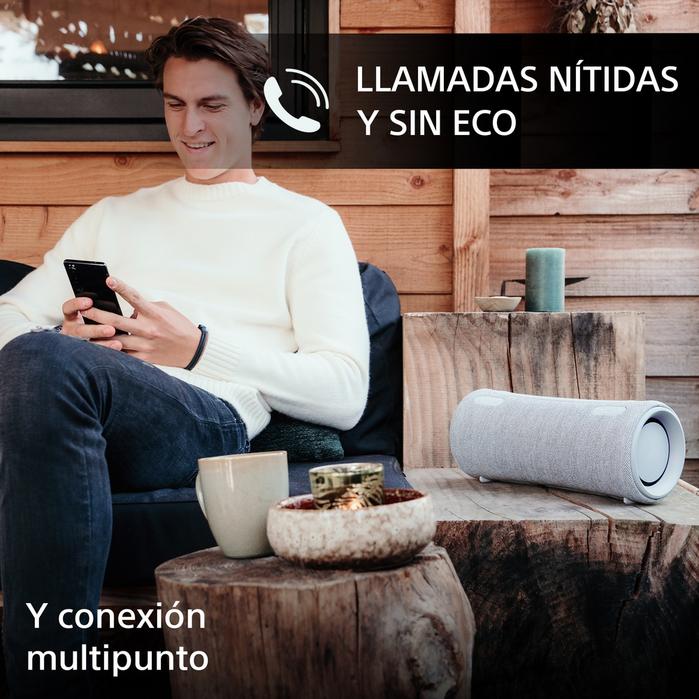 Hombre usando teléfono con un altavoz cerca, sentado en una estructura de madera.