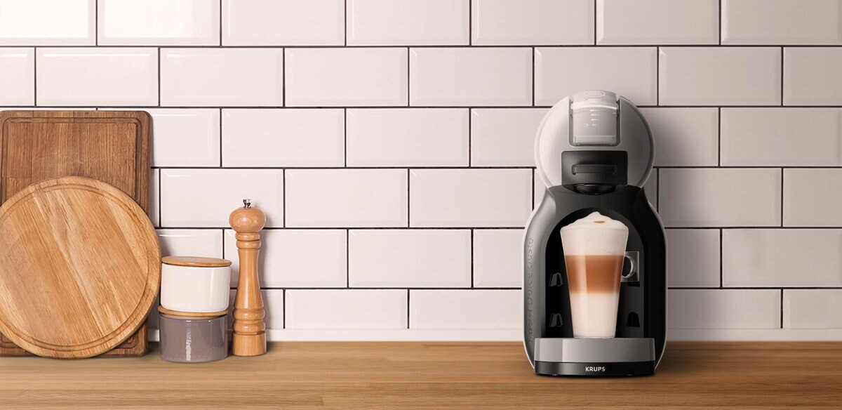 Ekspres do kawy z latte w szklance i drewniane deski do krojenia na białej kafelkowej ścianie.