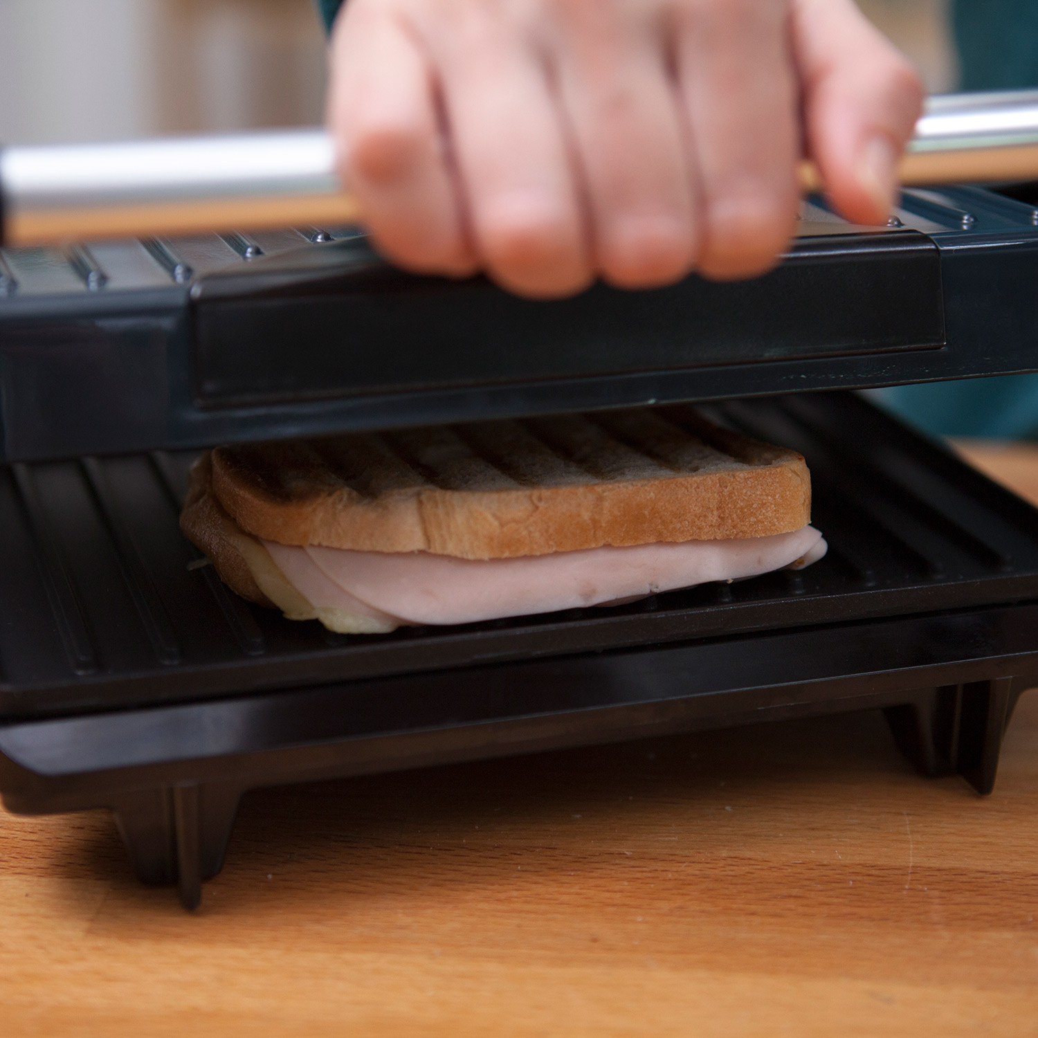 Un sándwich siendo prensado en una sandwichera negra sobre una superficie de madera.
