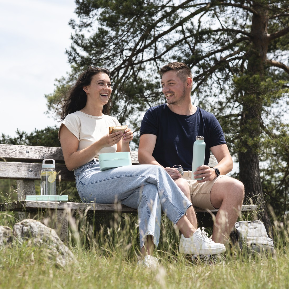 Un couple assis sur un banc, souriant, pique-niquant, profitant du plein air.