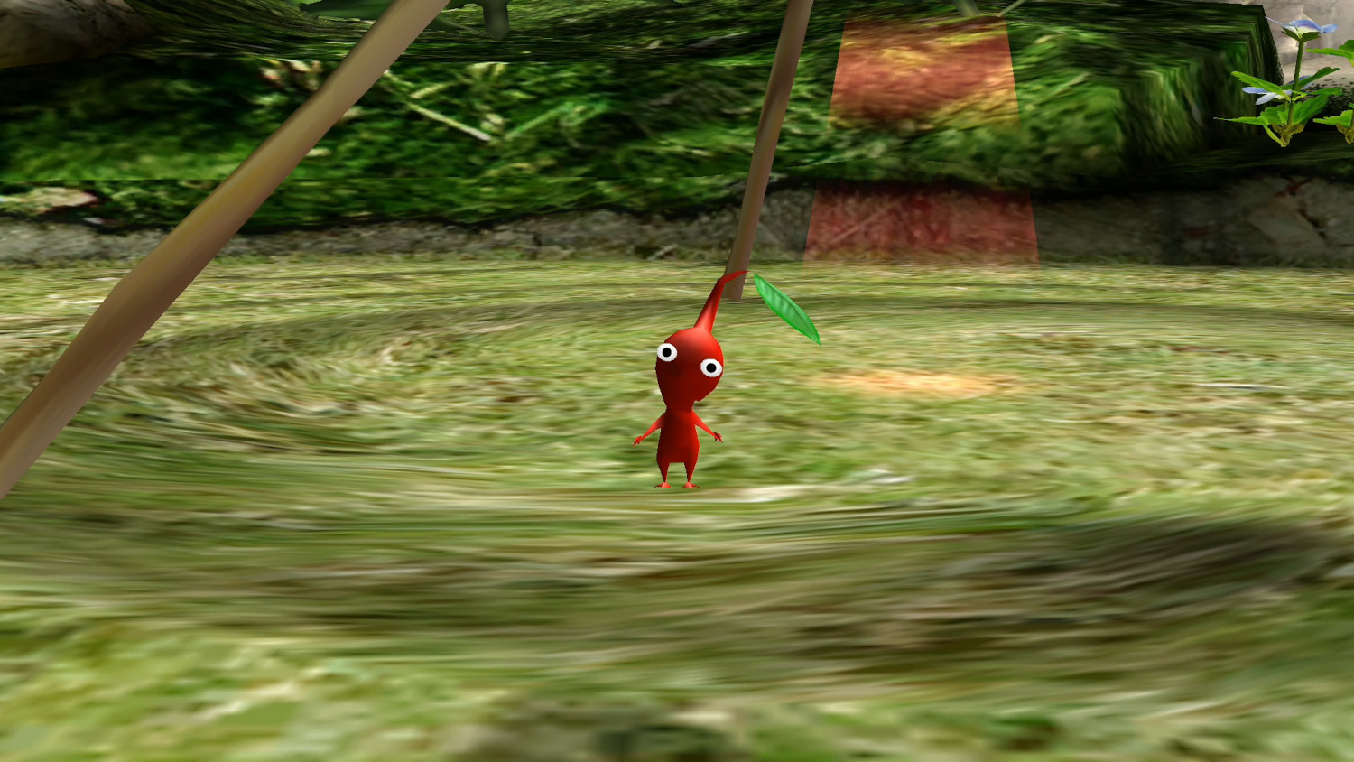 Un petit Pikmin rouge est suspendu à une branche dans un environnement vert luxuriant avec un arrière-plan flou.