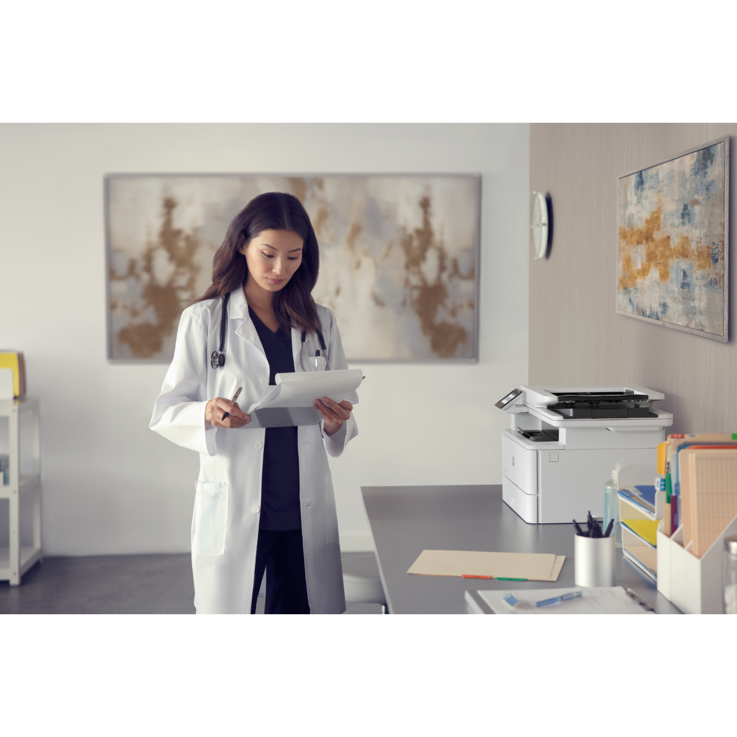 A doctor in a white coat reading papers in an office, with a printer and artwork.