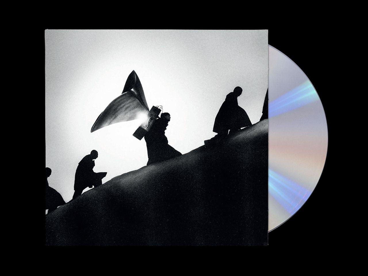 Schattenrisse von Figuren auf einem Hügel, die ein Kreuz tragen. Albumcover. CD daneben.