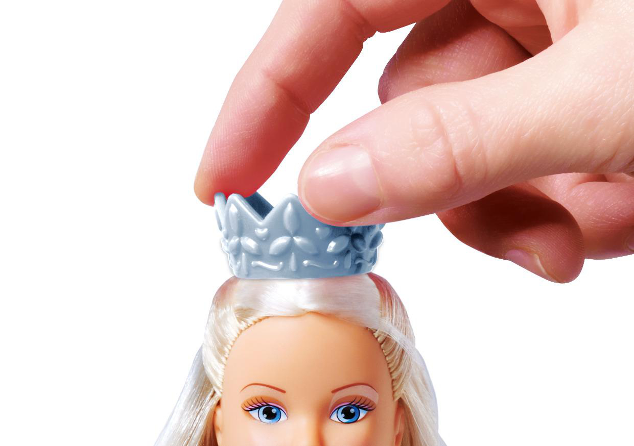 Eine Hand setzt einer Puppe eine Krone auf. Die Puppe hat blondes Haar und blickt nach oben.