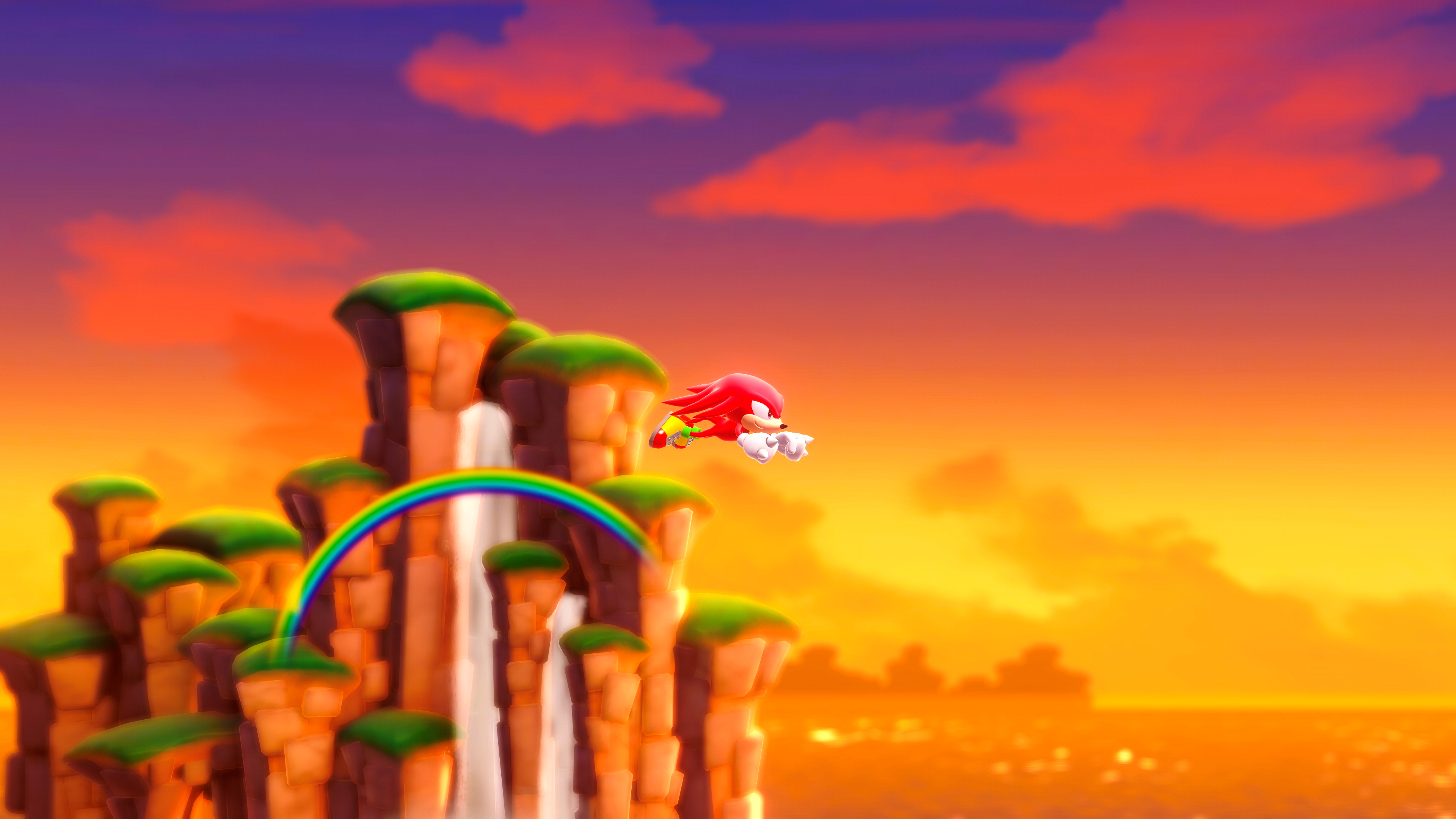 Una scena a cartoni animati di Knuckles che vola sopra un arcobaleno vicino a una cascata e un tramonto.