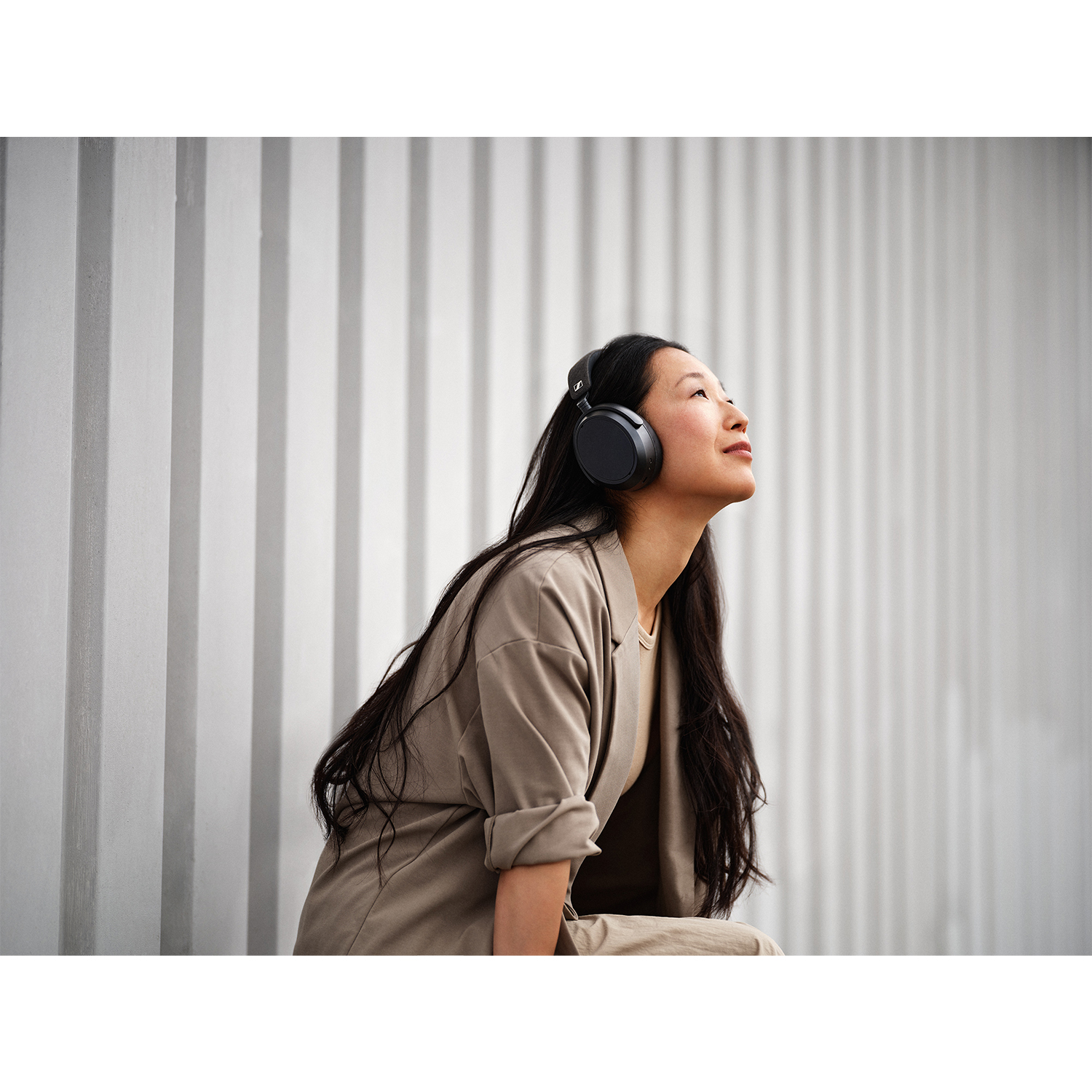 Una donna con cuffie nere guarda in su, indossando un cappotto beige chiaro.