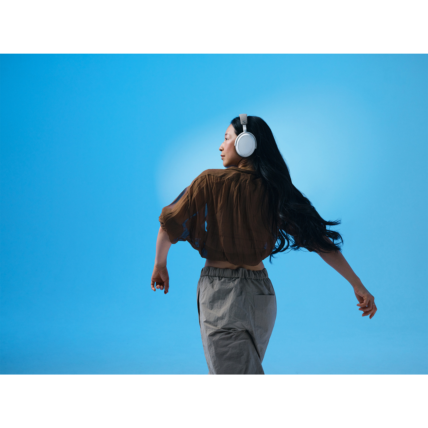 Una donna con capelli scuri con cuffie, di spalle, con le braccia tese contro uno sfondo blu.