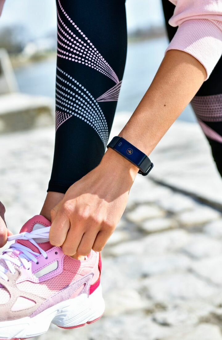 Osoba zawiązująca sznurowadło. Ma na nadgarstku opaskę fitness i różowo-czarny strój sportowy.