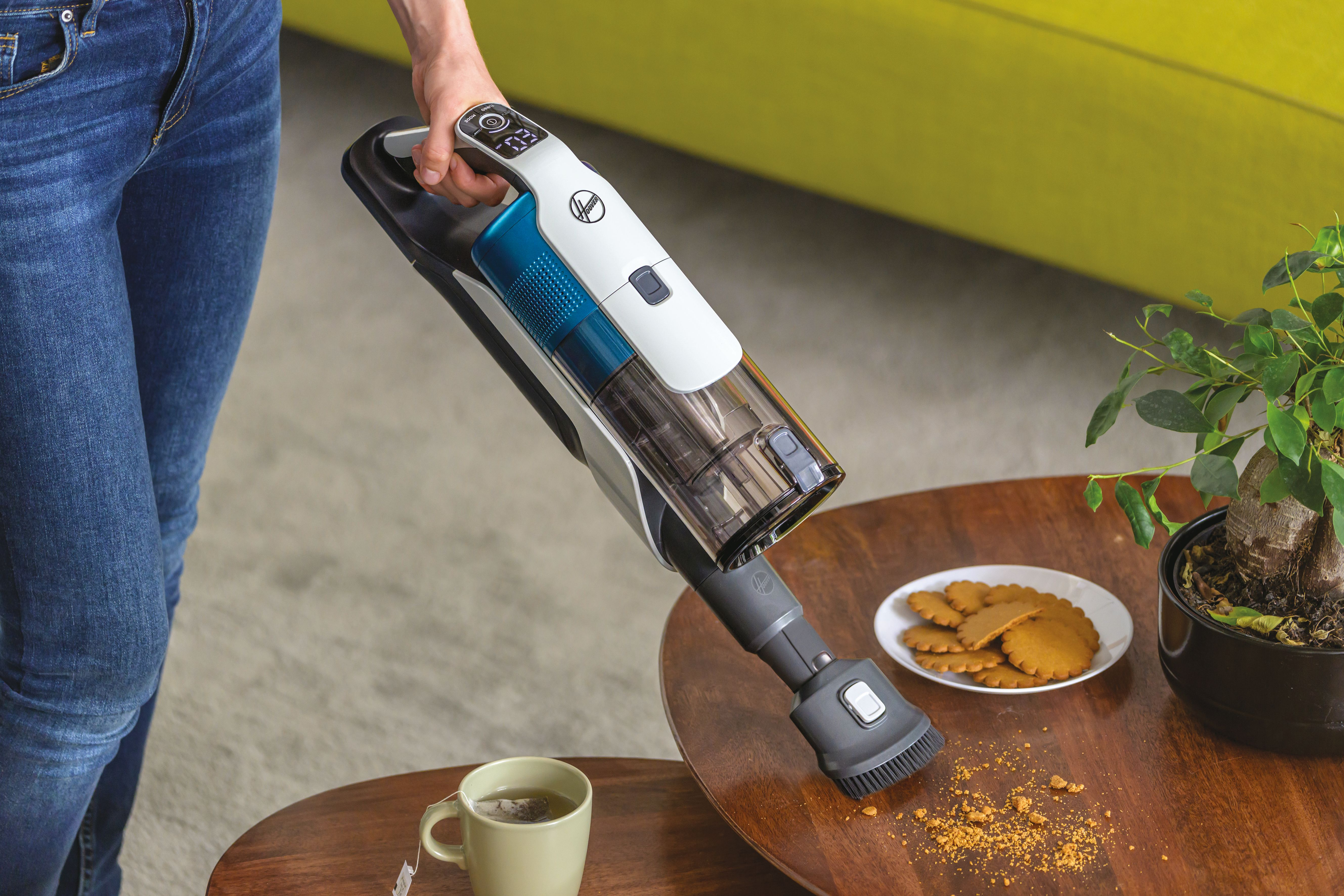 Una persona usando una aspiradora de mano Hoover, limpiando migas sobre una mesa de madera.