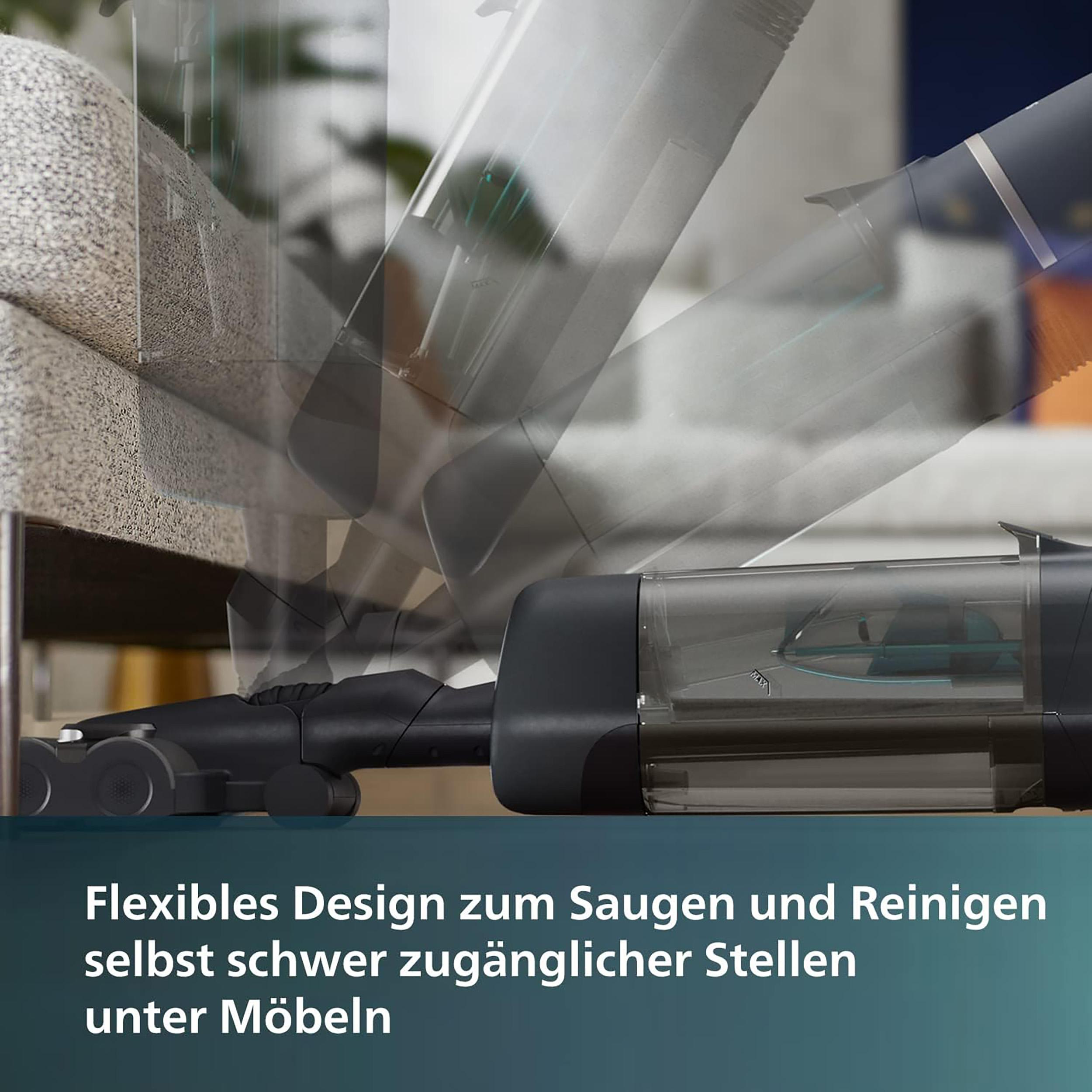 Ein Staubsauger wird beim Reinigen unter Möbeln demonstriert. Text auf Deutsch sichtbar.