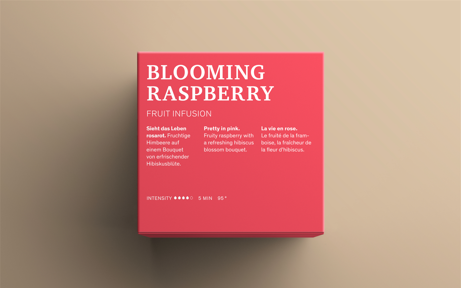 Rote Box mit Text: BLOOMING RASPBERRY und Beschreibungen auf Englisch, Deutsch und Französisch. Beiger Hintergrund.