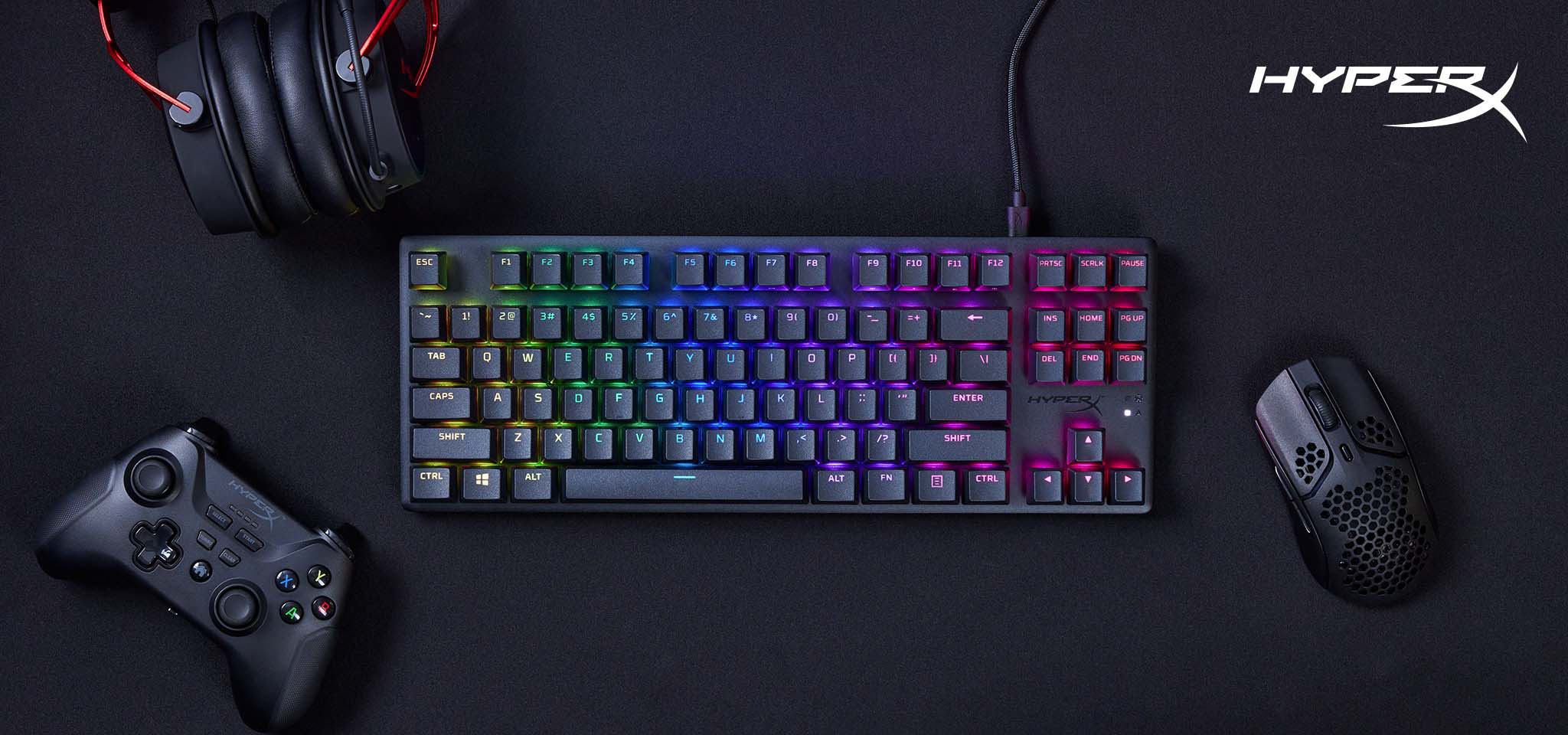 Un teclado, un ratón y un mando HyperX están sobre una superficie negra.