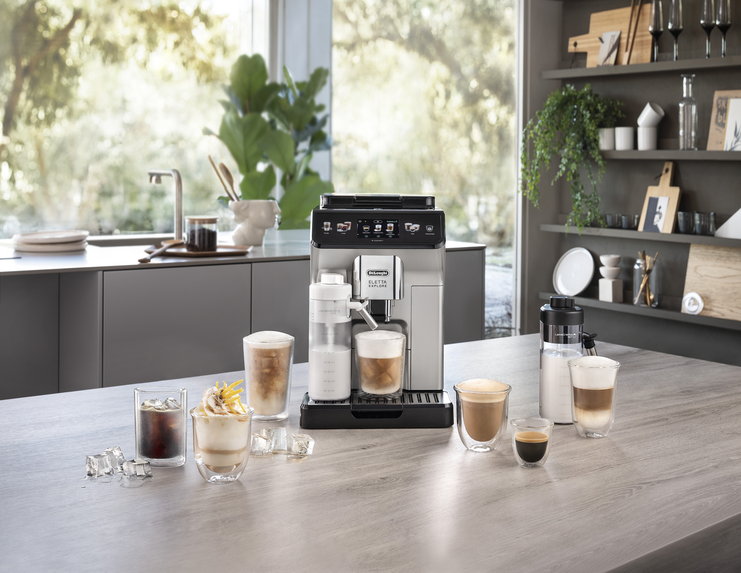 Una cafetera con varias bebidas de café y la cocina de una persona con plantas de fondo.