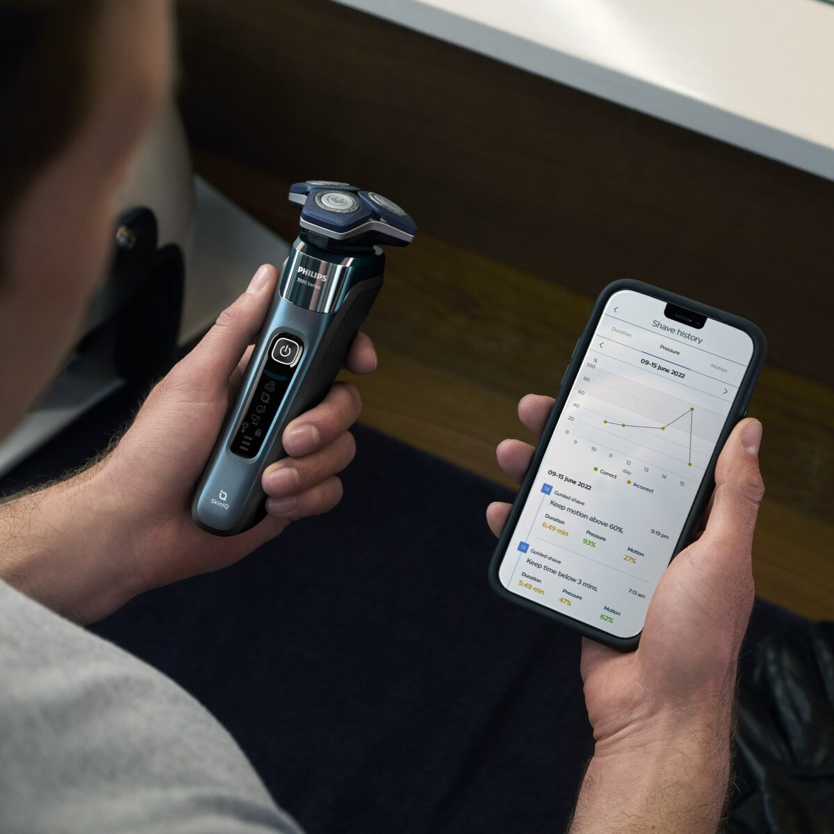 Mężczyzna trzymający golarkę elektryczną i telefon wyświetlający wykres danych historii golenia.