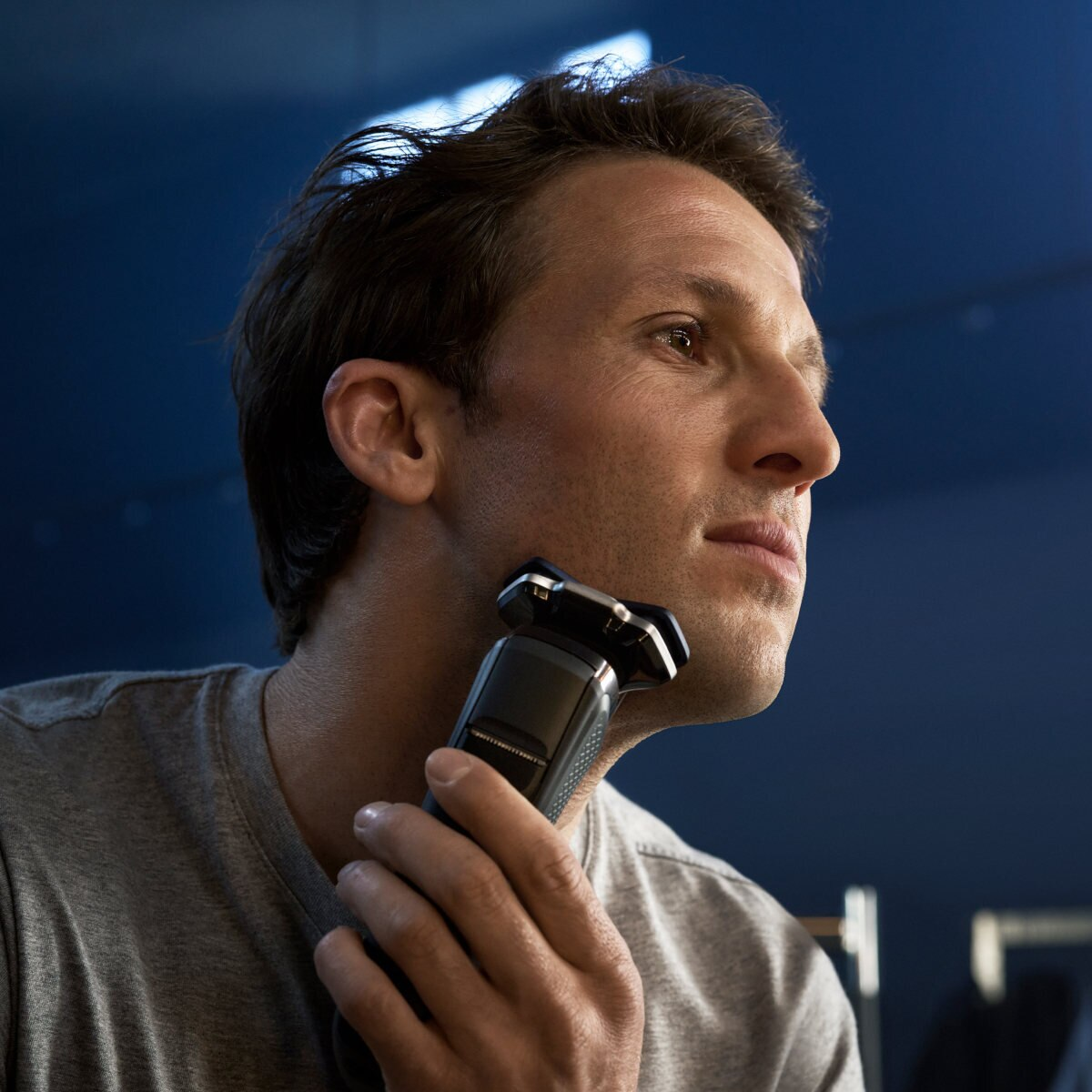 Mężczyzna goli twarz czarną golarką elektryczną na niebieskim tle.