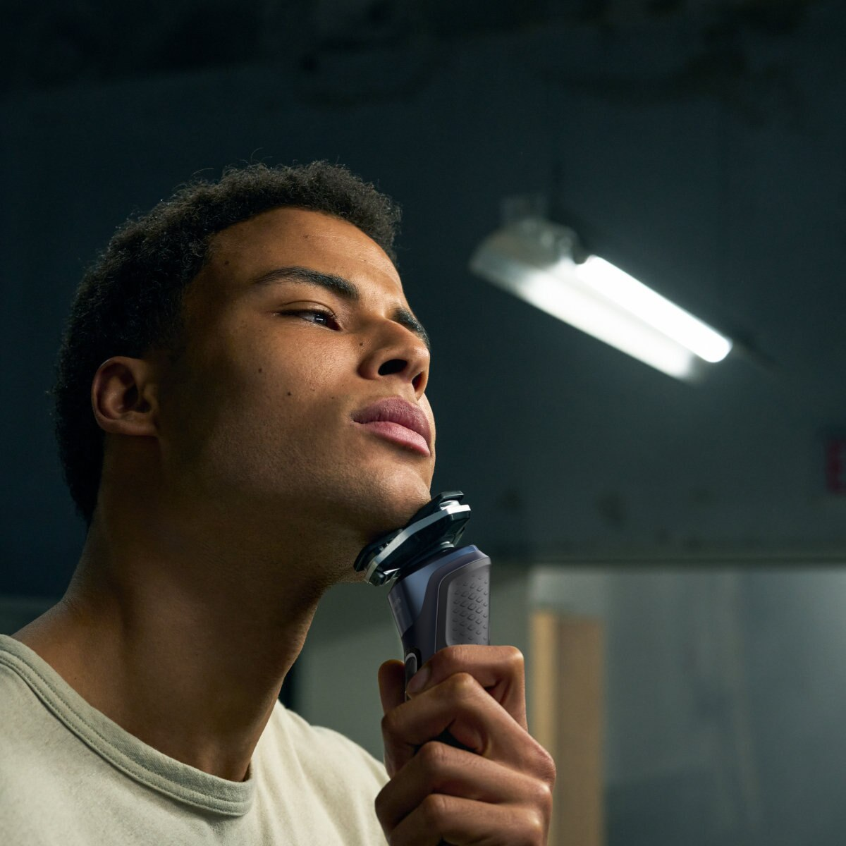 Mężczyzna goli twarz golarką elektryczną na ciemnym tle.