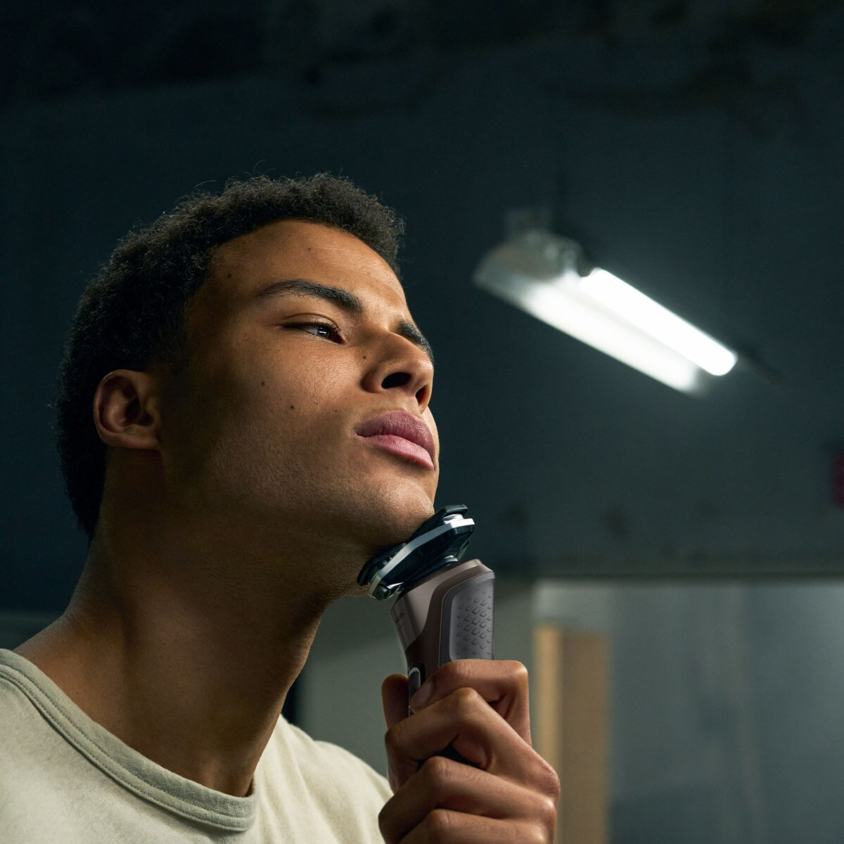 Mężczyzna goli twarz golarką elektryczną, zbliżenie, w otoczeniu łazienki.